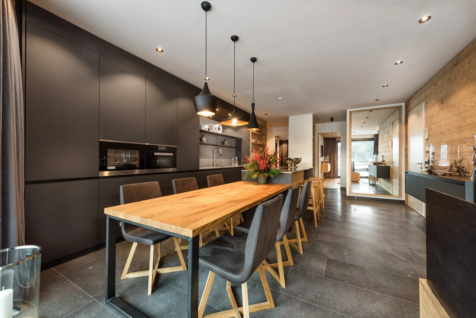 Un comedor moderno tiene una larga mesa de madera bajo lámparas colgantes.
