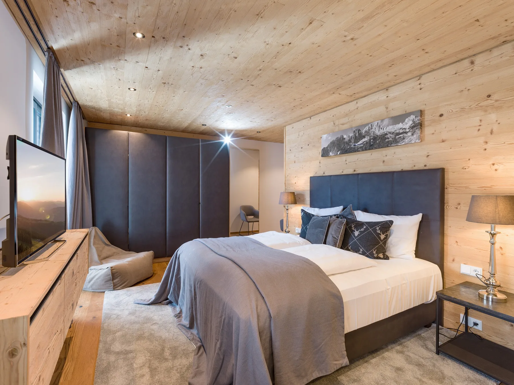 Un dormitorio con una cama grande, ropa de cama gris y un interior de madera clara.