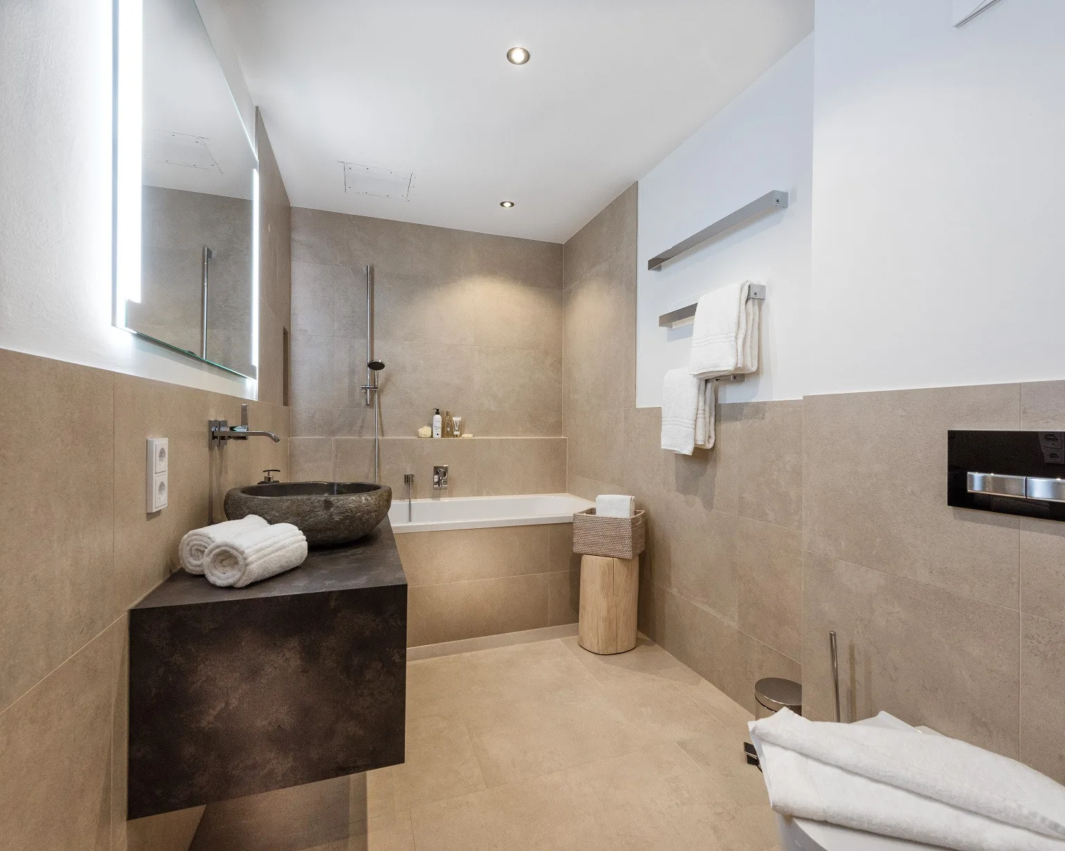 Un baño revestido de azulejos con bañera, ducha y lavabo sobre una encimera oscura.