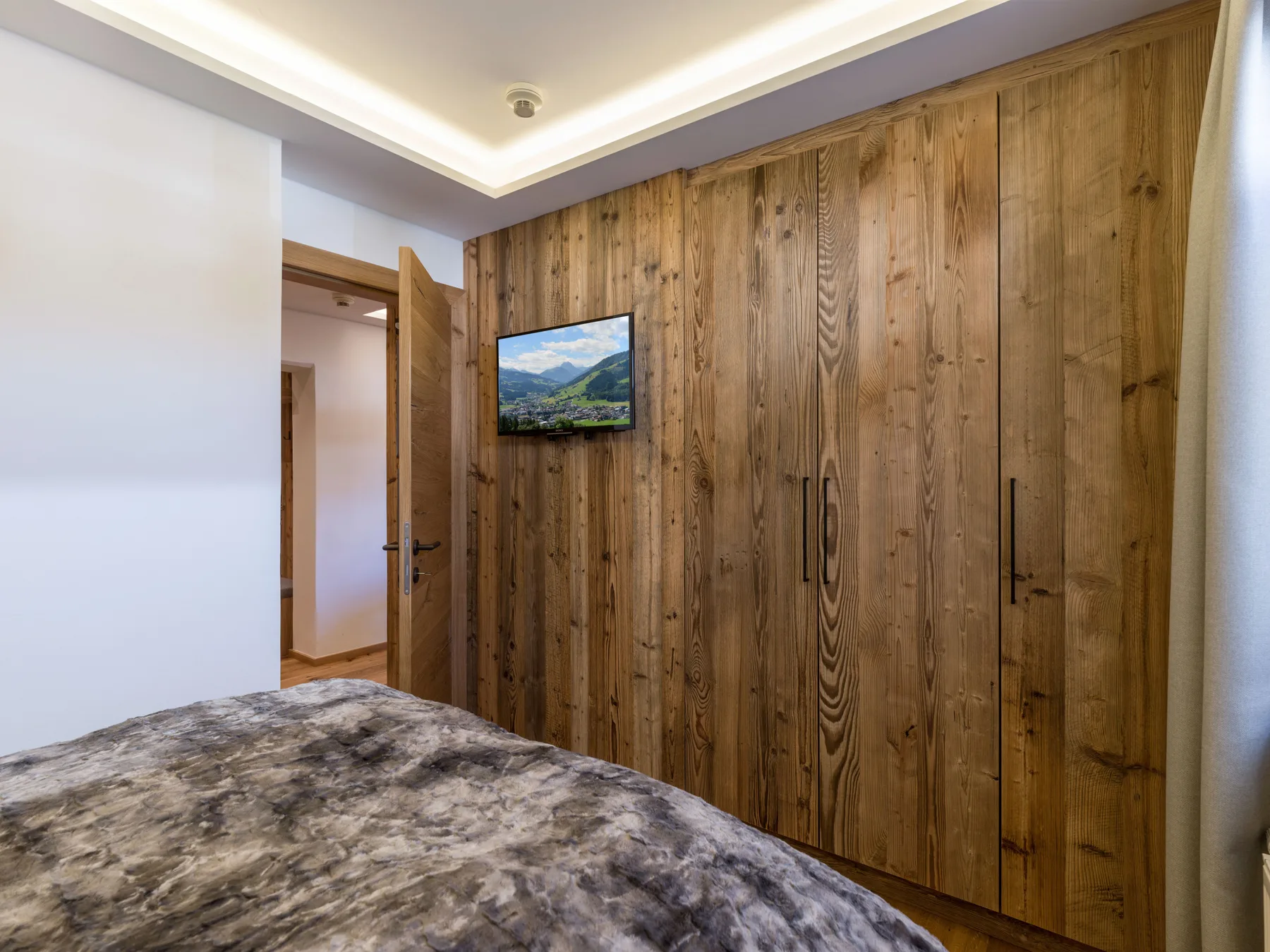 Bedroom with a bed beside a wooden wardrobe and wall-mounted television.