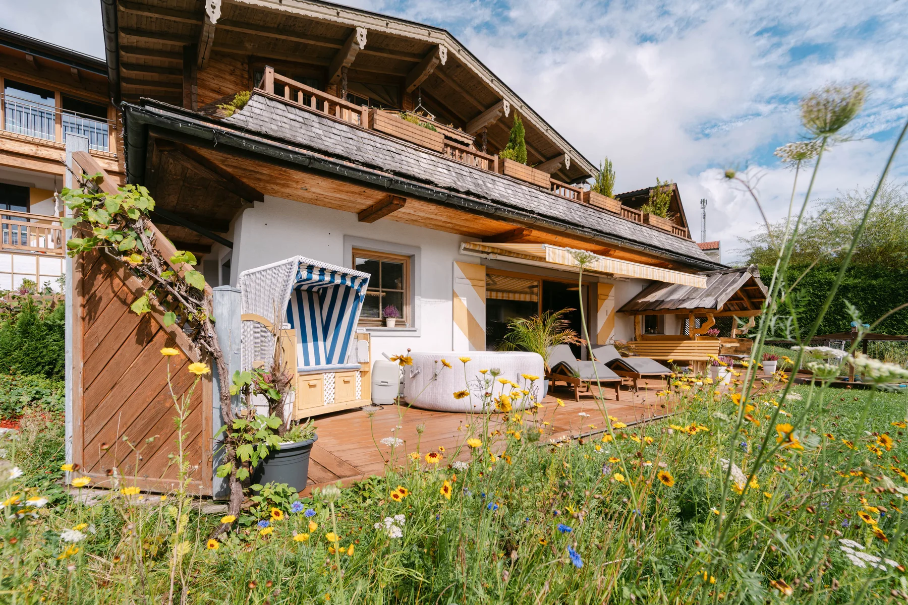 Una casa de estilo chalet con terraza de madera, asientos al aire libre y jardín florido.