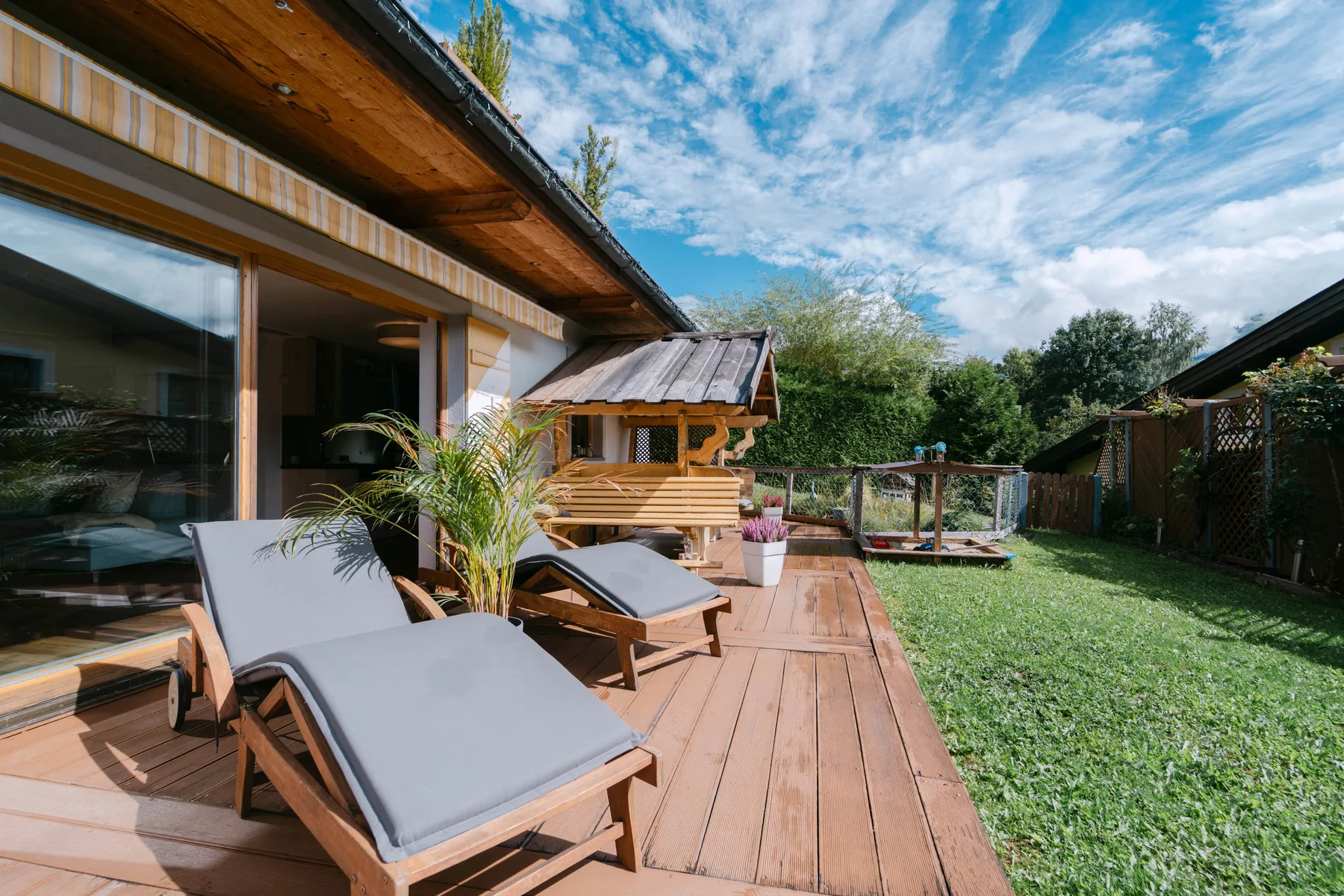 Una terraza de madera con asientos reclinables da a una zona exterior con césped.