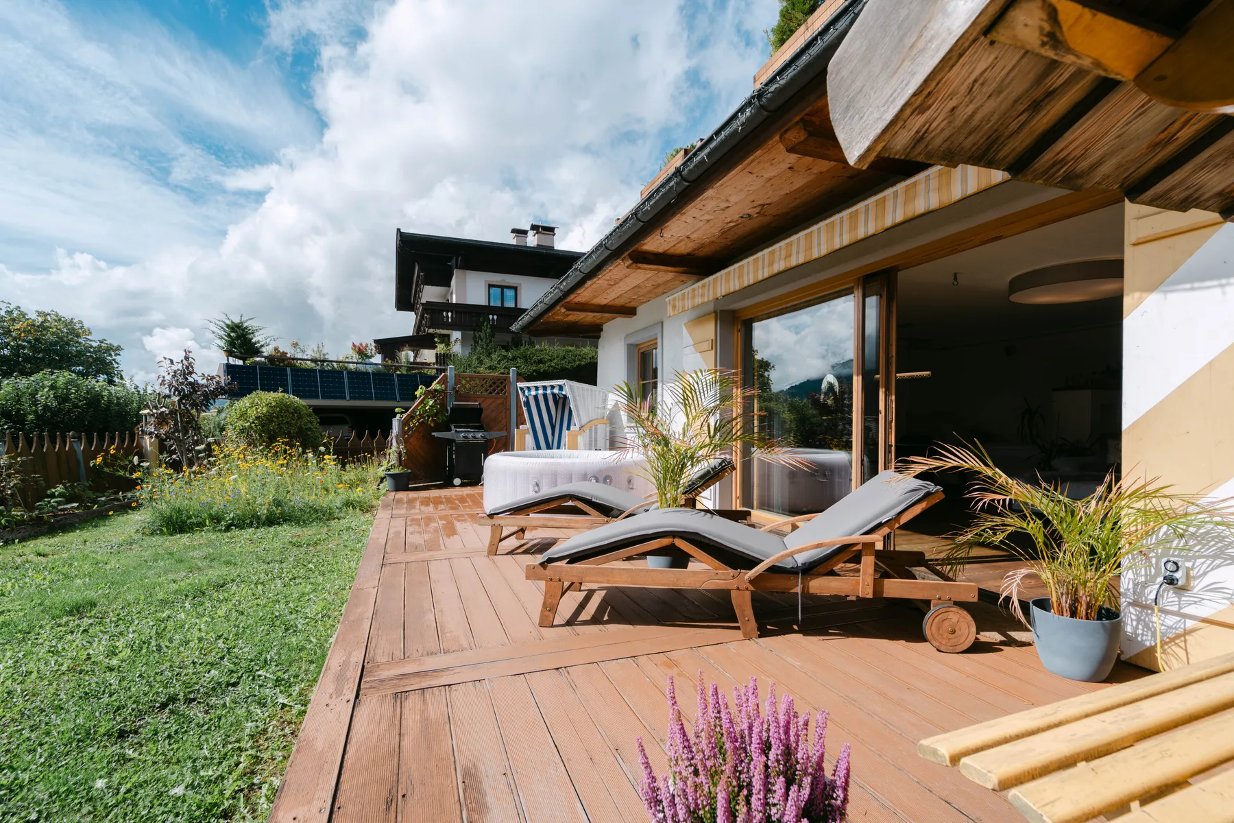Una terraza de madera con asientos al aire libre y plantas en macetas junto a una casa.
