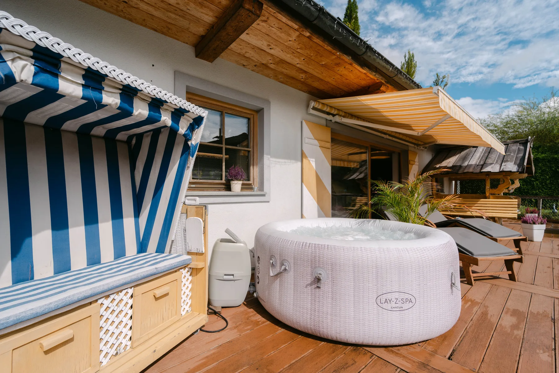 Una terraza de madera con una bañera de hidromasaje redonda, asientos a rayas y un toldo retráctil.