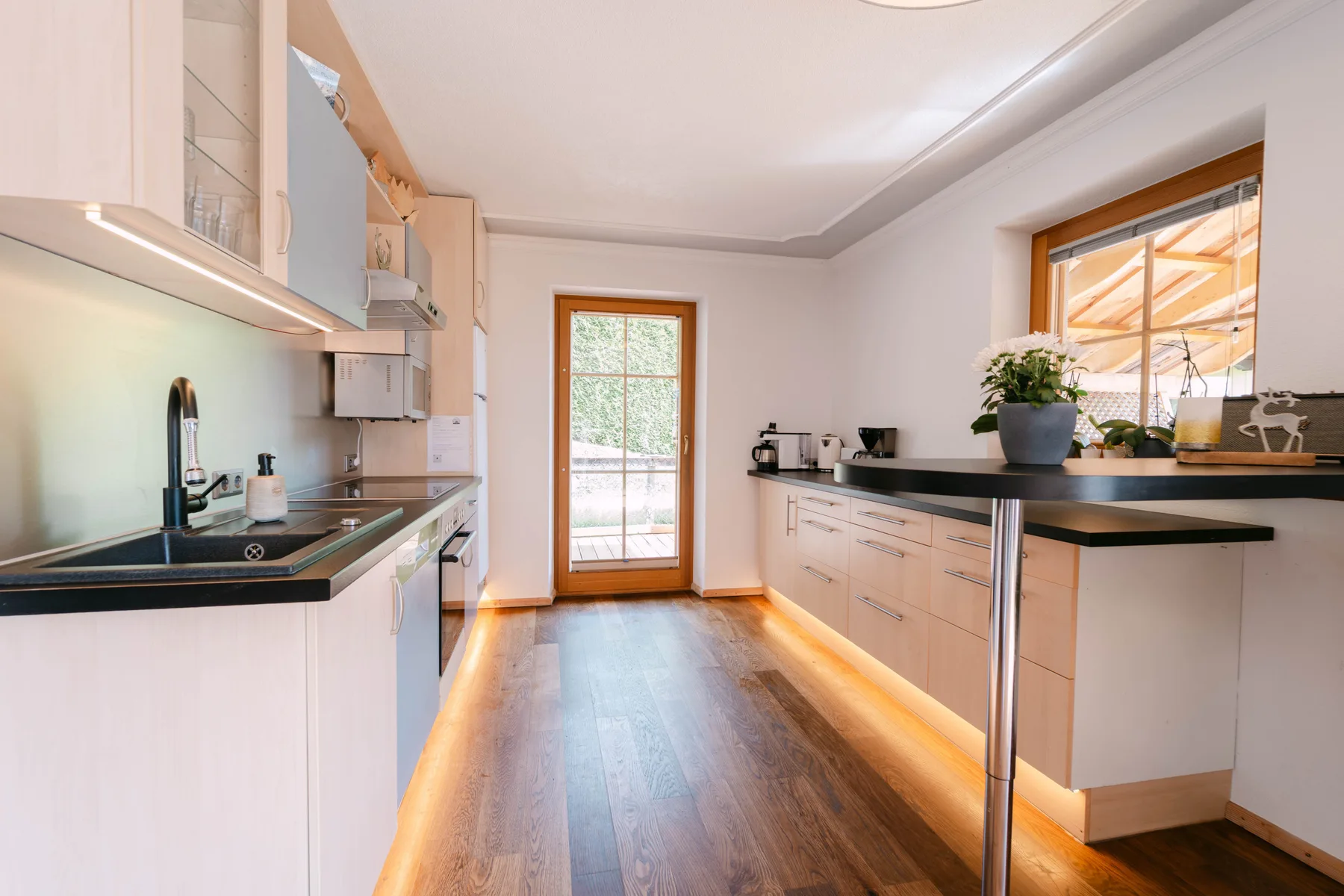 Una cocina luminosa con gabinetes claros, encimeras oscuras y una puerta de vidrio.