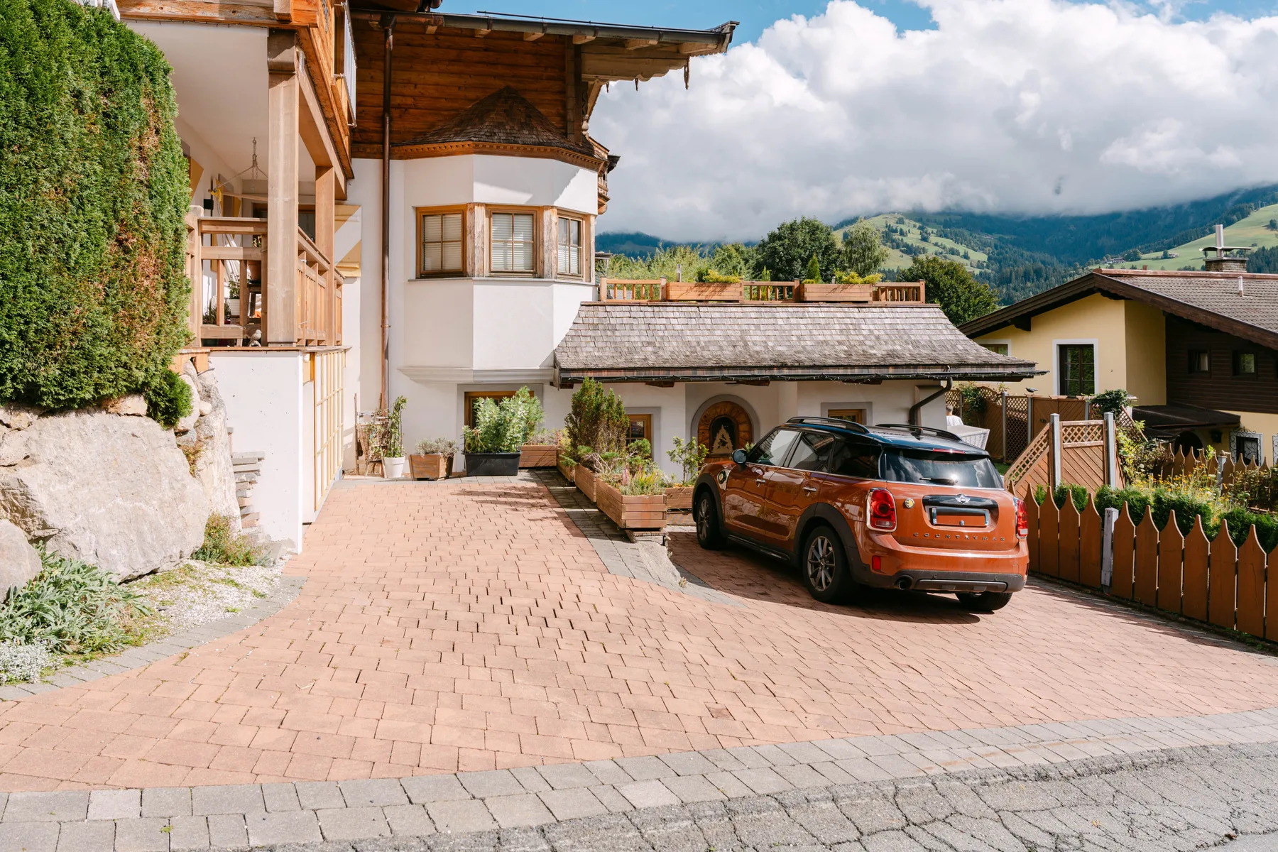 Zona común: Una entrada pavimentada frente a un edificio, con un coche estacionado y vistas a las montañas.