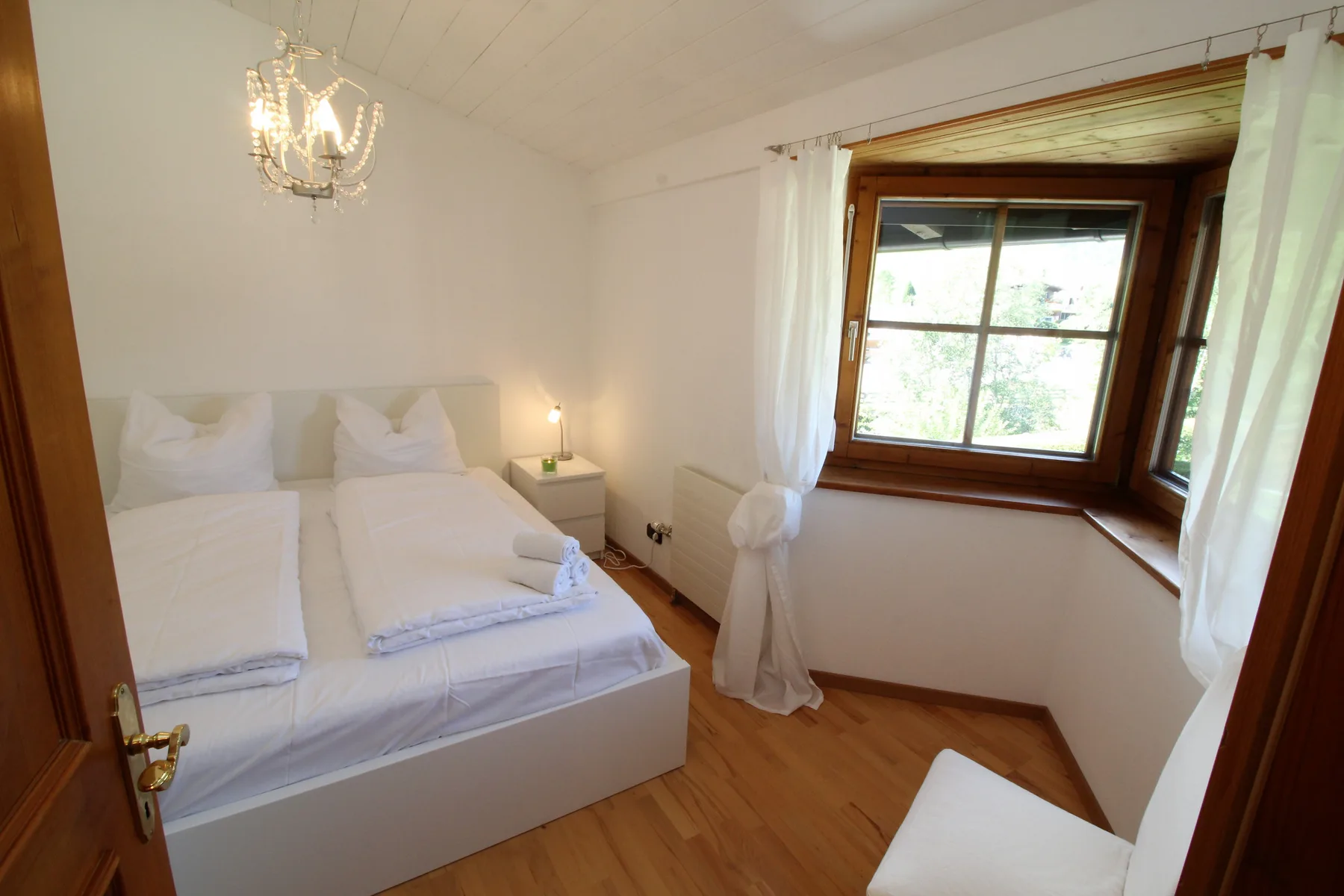 Un dormitorio luminoso con ropa de cama blanca y una gran ventana enmarcada en madera.