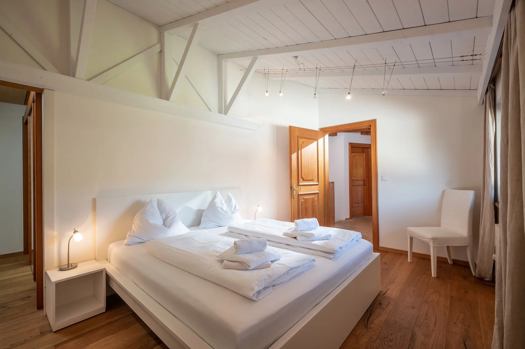 Un dormitorio luminoso con una cama grande, ropa de cama blanca y suelo de madera.