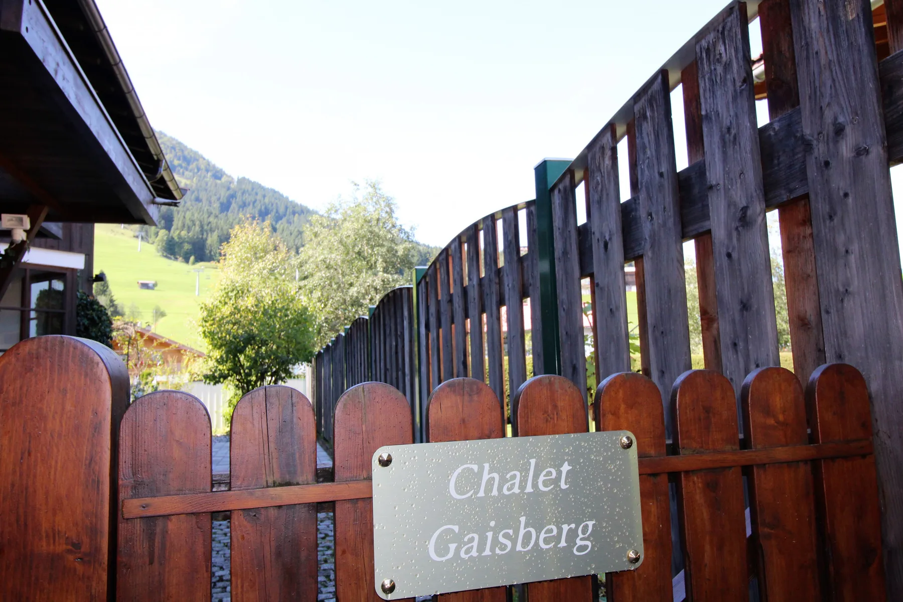 Una cerca de madera con un letrero de chalet está junto a una ladera verde.