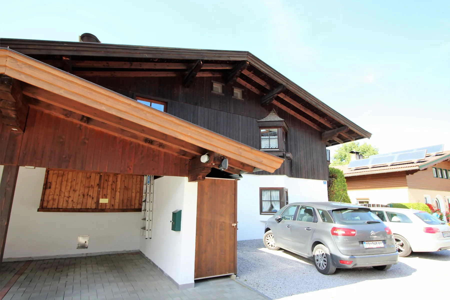Un edificio de madera oscura con una entrada cubierta y coches estacionados afuera.
