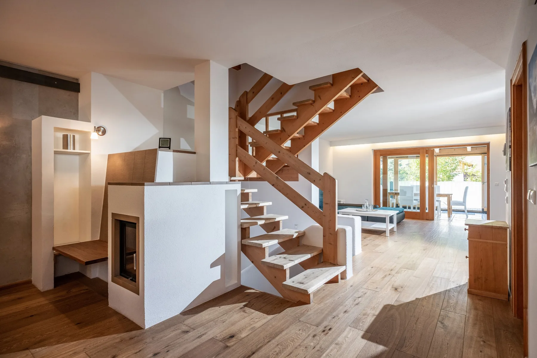 Una sala de planta abierta con una escalera de madera y comedor junto a grandes ventanales.