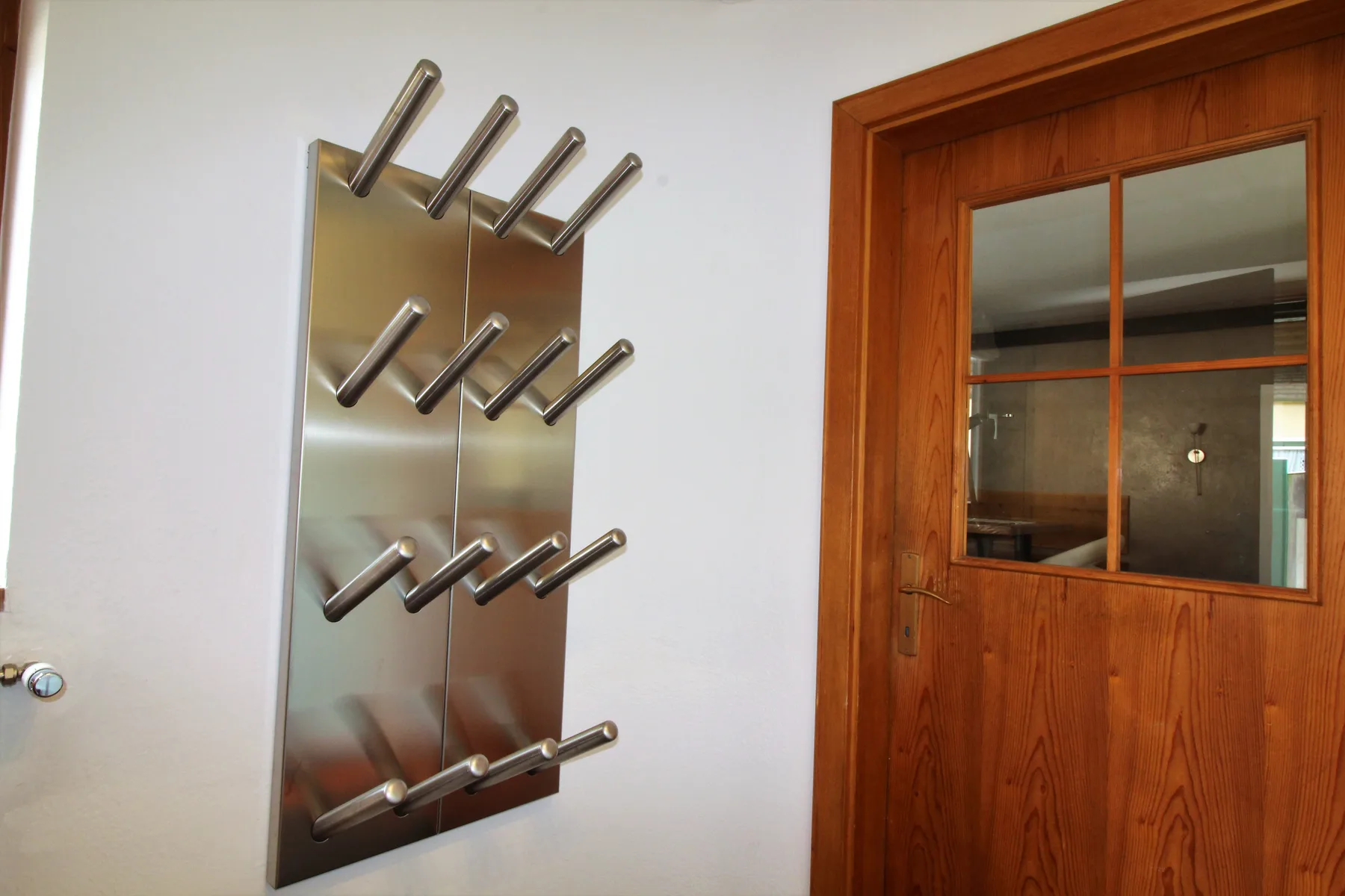 Una puerta de madera con paneles de vidrio está junto a un perchero metálico de pared.