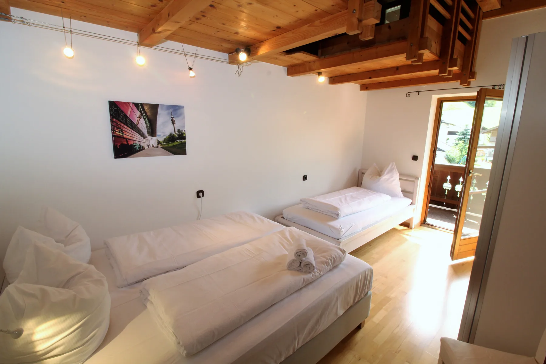 Un dormitorio con dos camas bajo un techo de madera, con salida a un balcón.