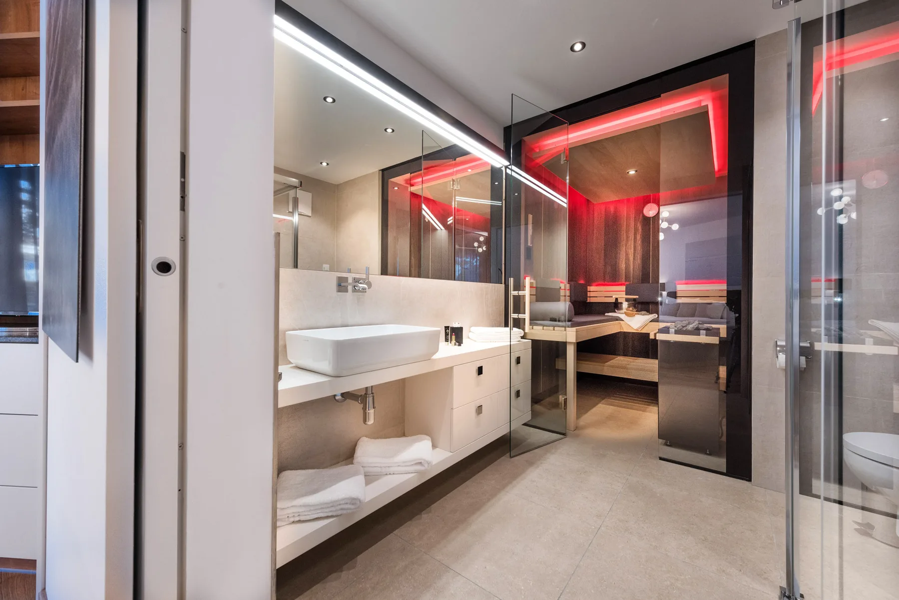 Un baño moderno con un tocador largo, lavabo sobre encimera y ducha de vidrio.