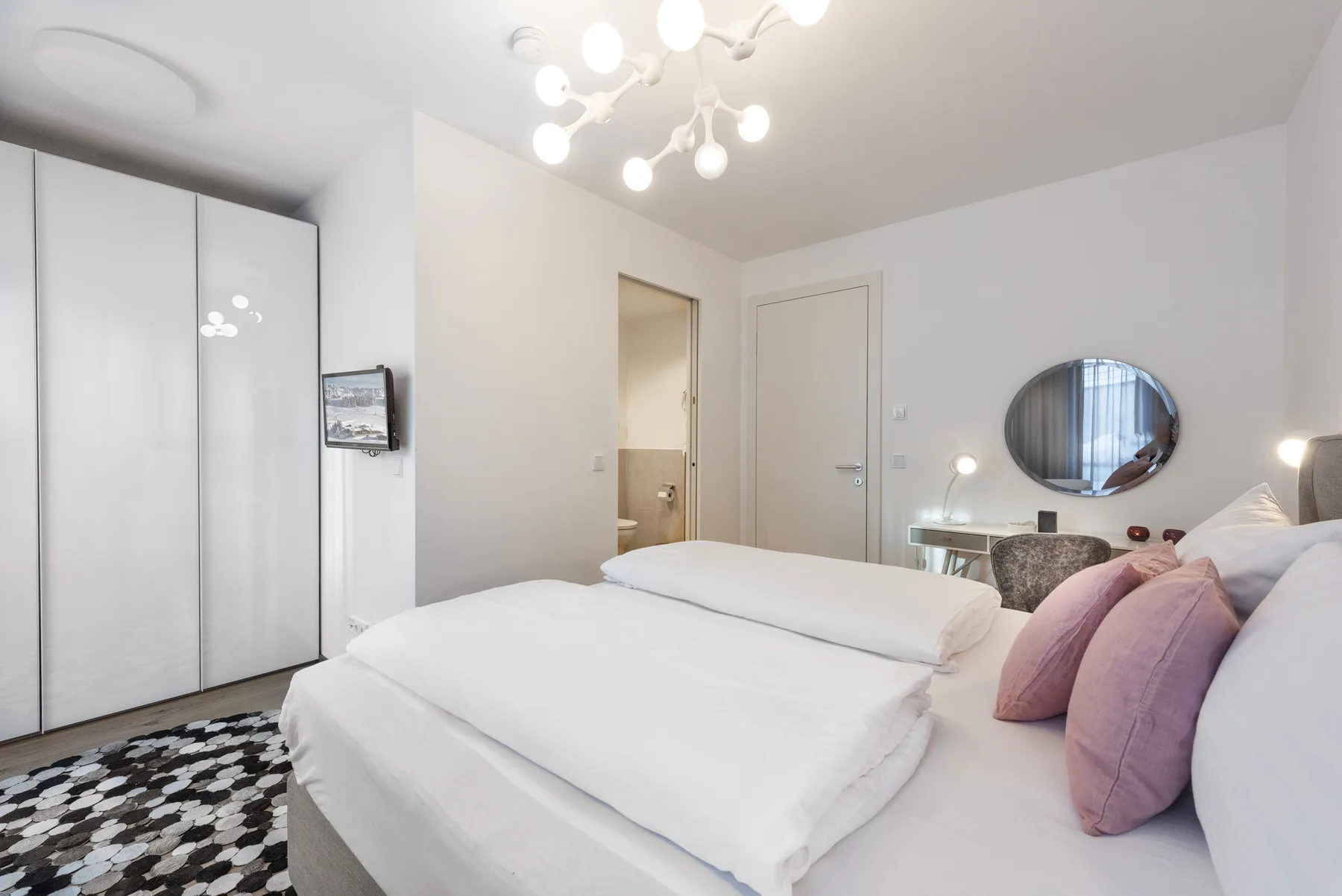 Un dormitorio luminoso con una cama blanca y un armario con espejo.
