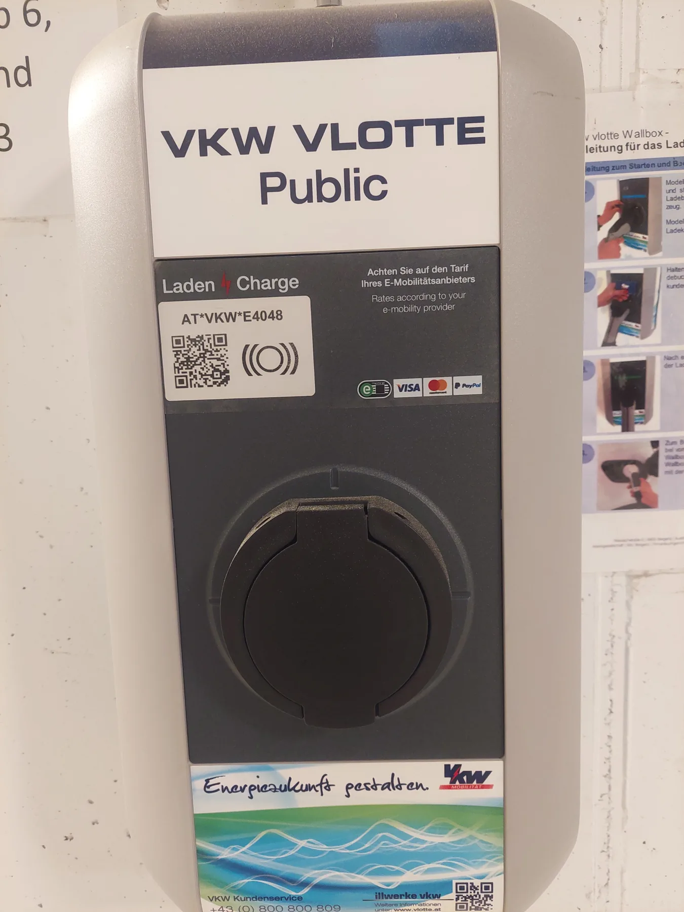 Zona común: Un punto público de carga para vehículos eléctricos montado en la pared, con una toma de carga.