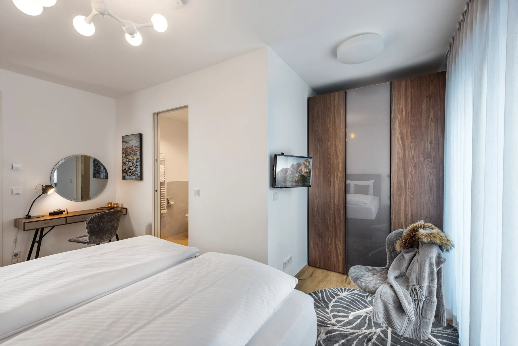 Un dormitorio con una cama, un escritorio y un armario junto a la ventana.