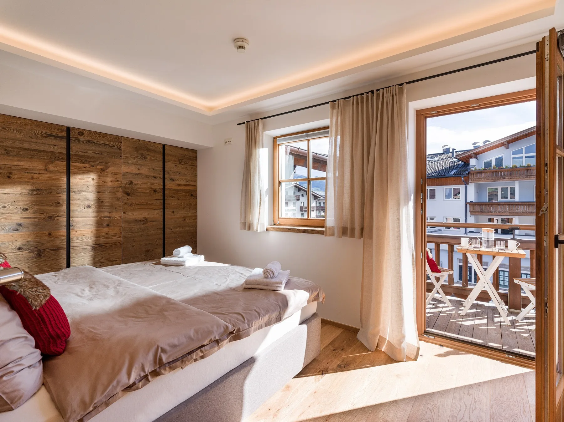 Un dormitorio iluminado por el sol, con una cama junto a una puerta abierta al balcón y ventanas.
