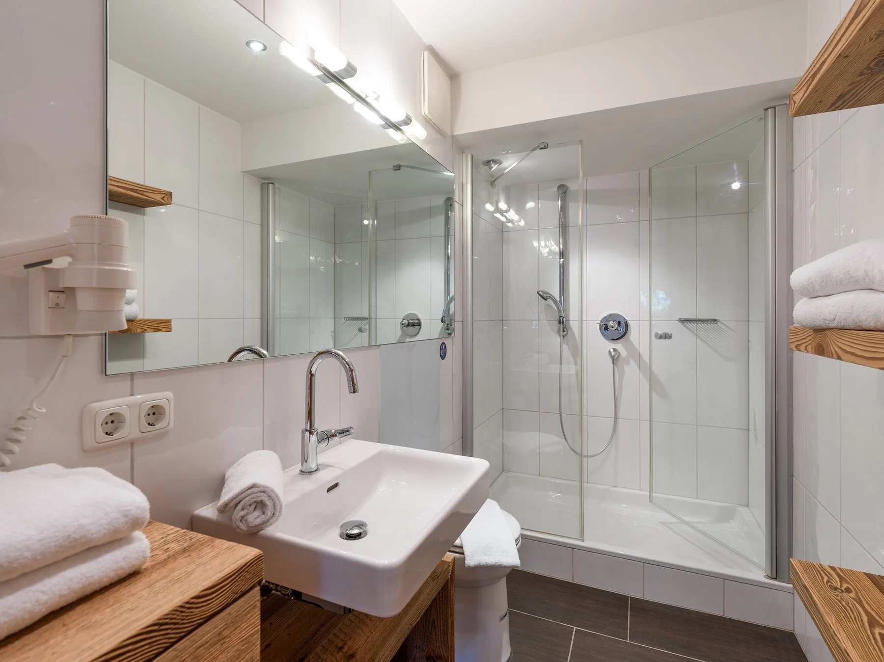 Un baño luminoso con azulejos cuenta con un lavabo y una ducha de vidrio.