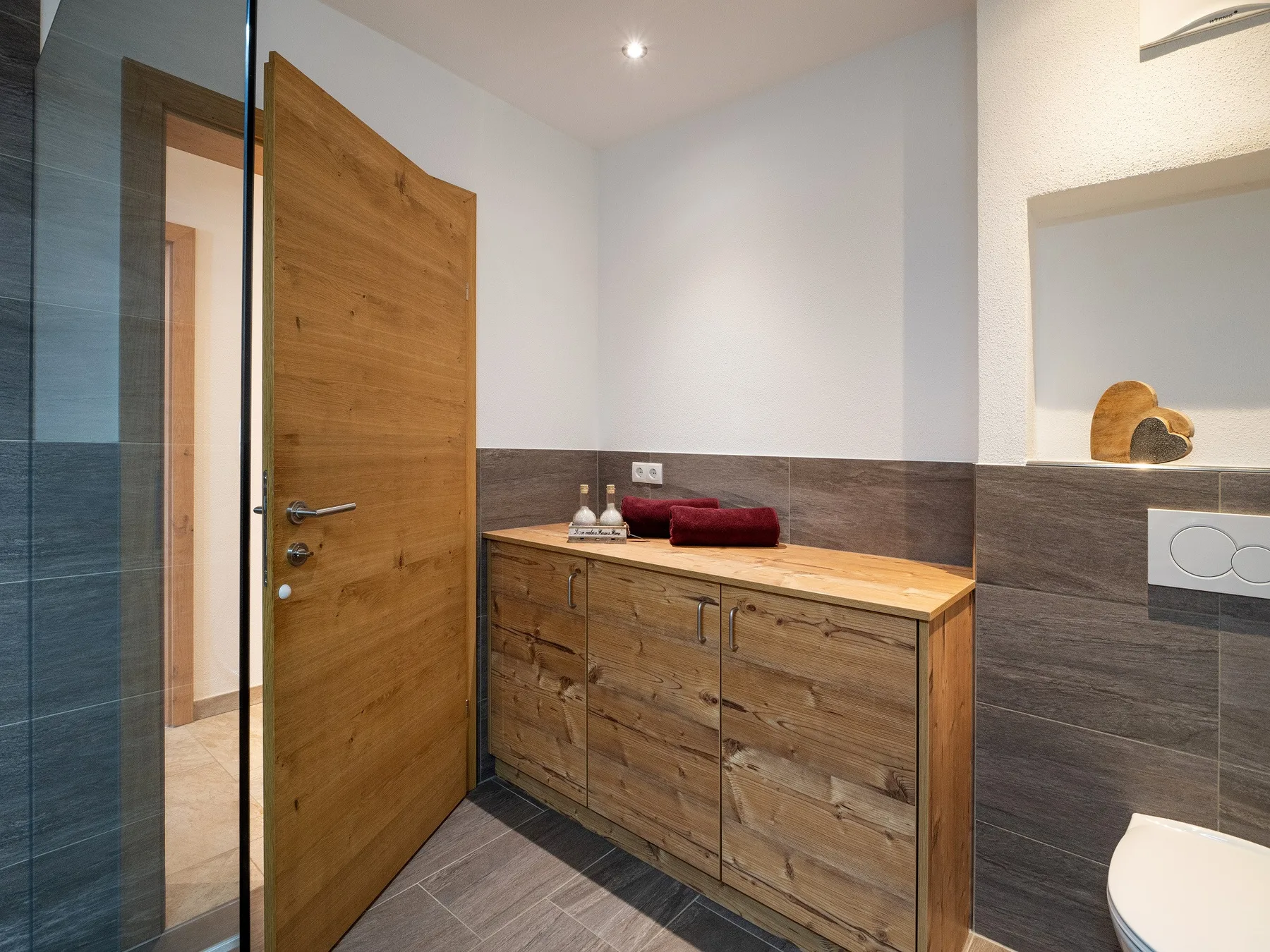 Un lavabo de baño con mueble de madera está junto a una puerta de madera abierta.