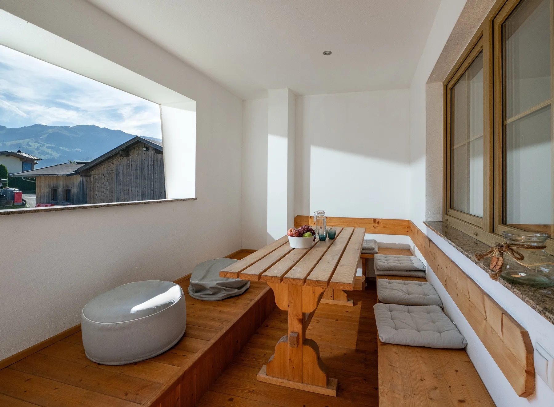 Un luminoso rincón de comedor con mesa de madera y asientos con banco junto a grandes ventanas.