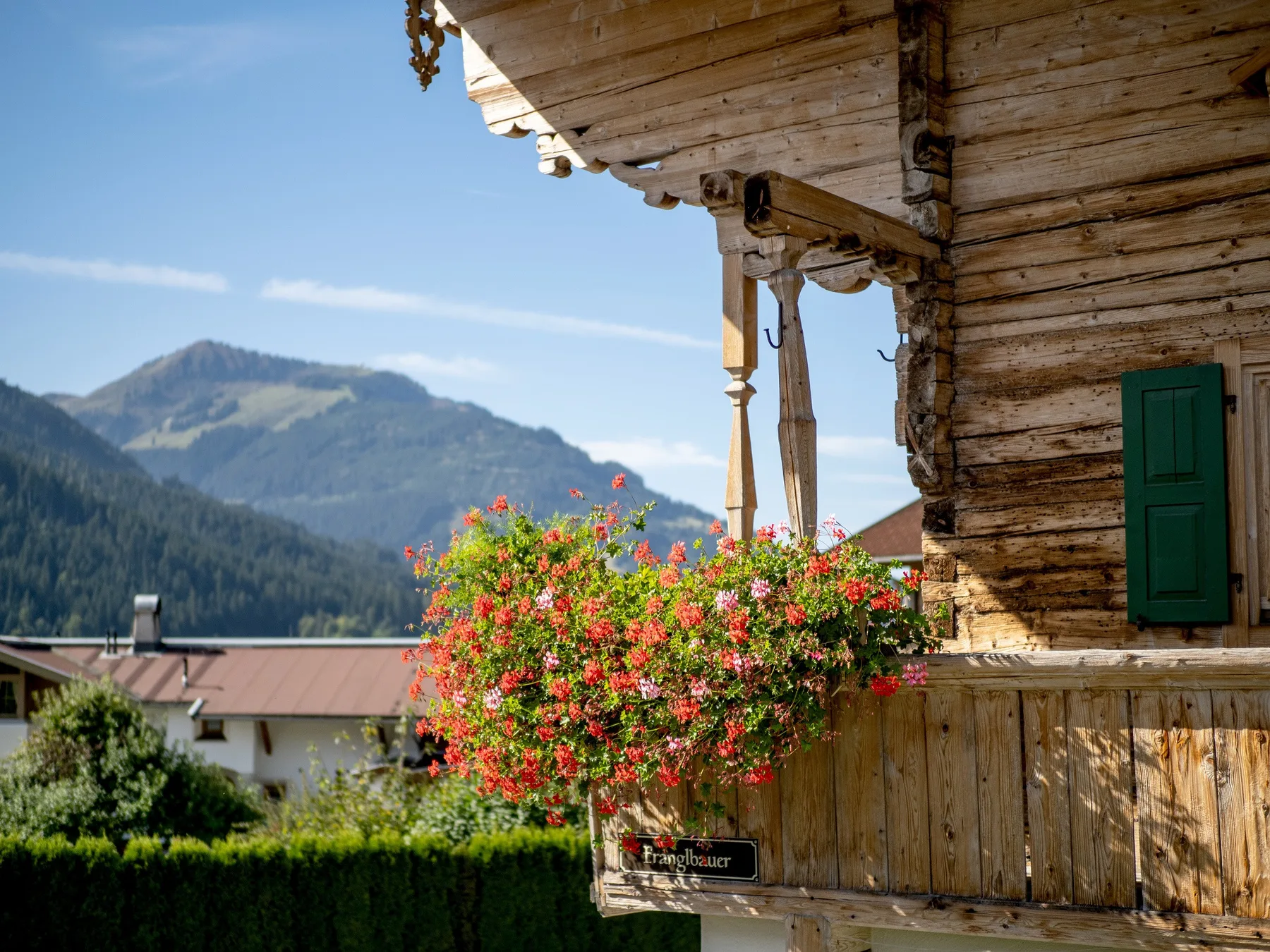 Un balcón de madera con flores rojas da a un paisaje montañoso.