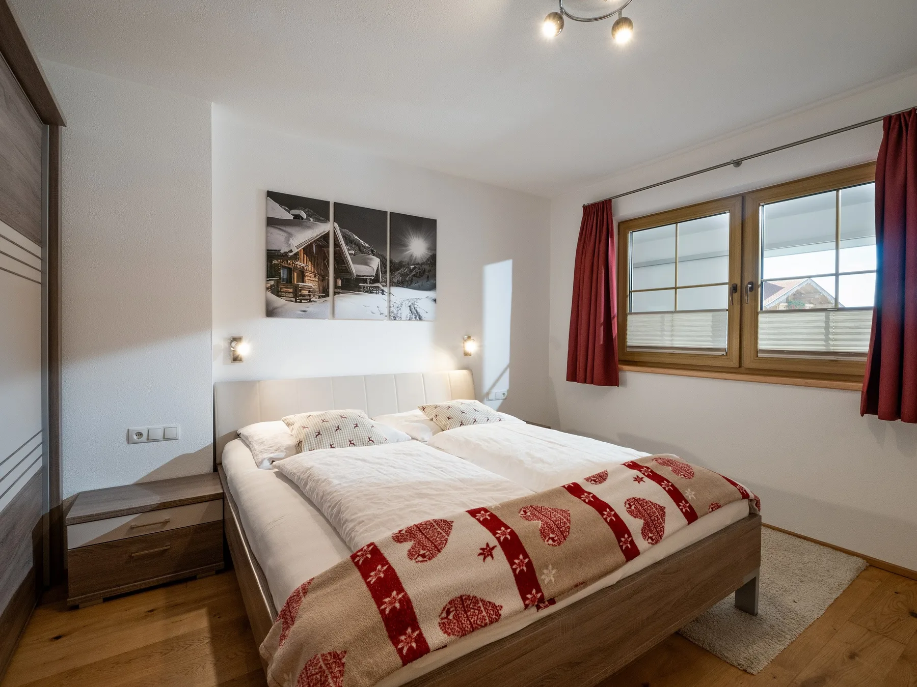 Un dormitorio con una cama doble, ropa de cama estampada y una ventana con cortinas rojas.