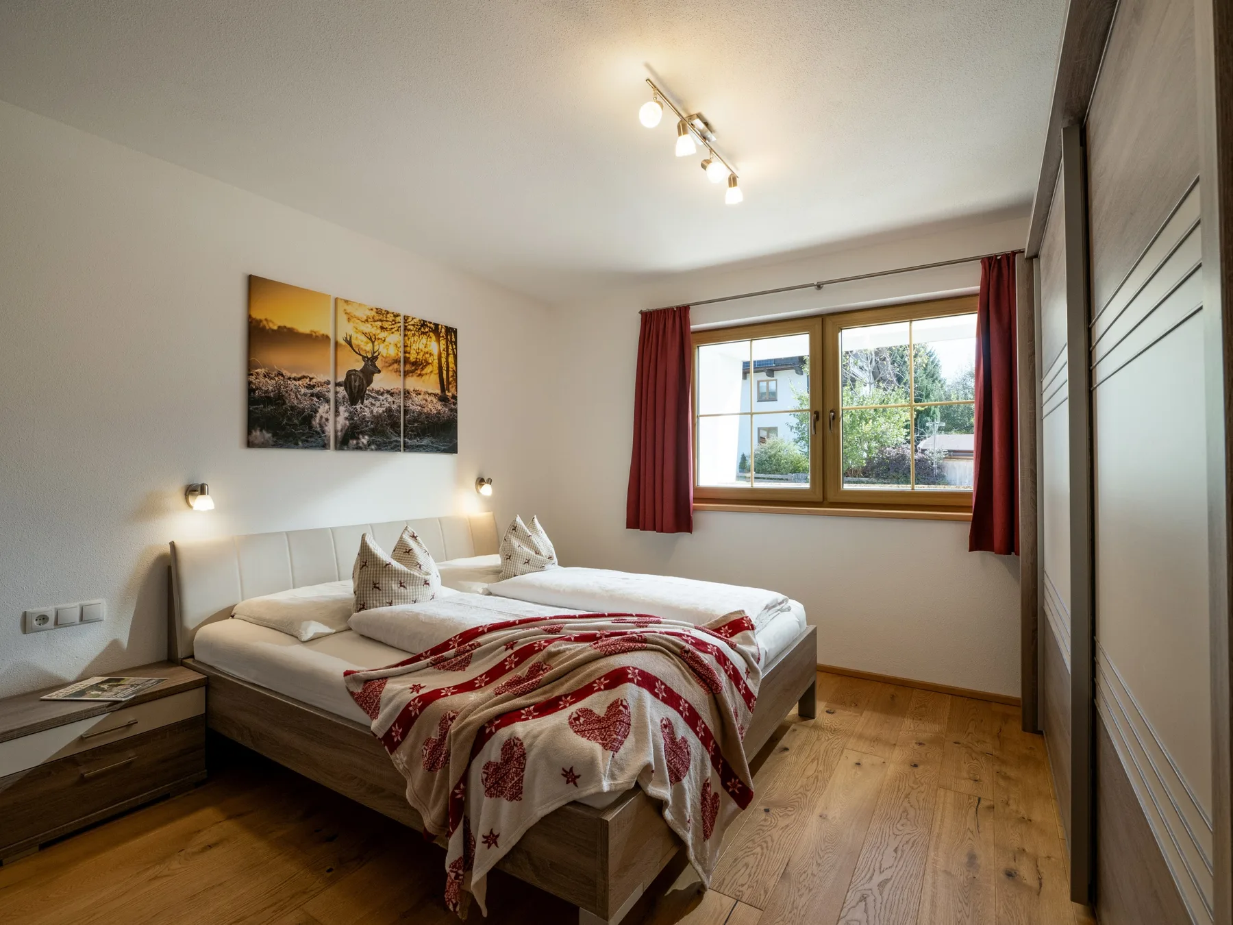 Un dormitorio luminoso con dos camas, cortinas rojas y una ventana grande.
