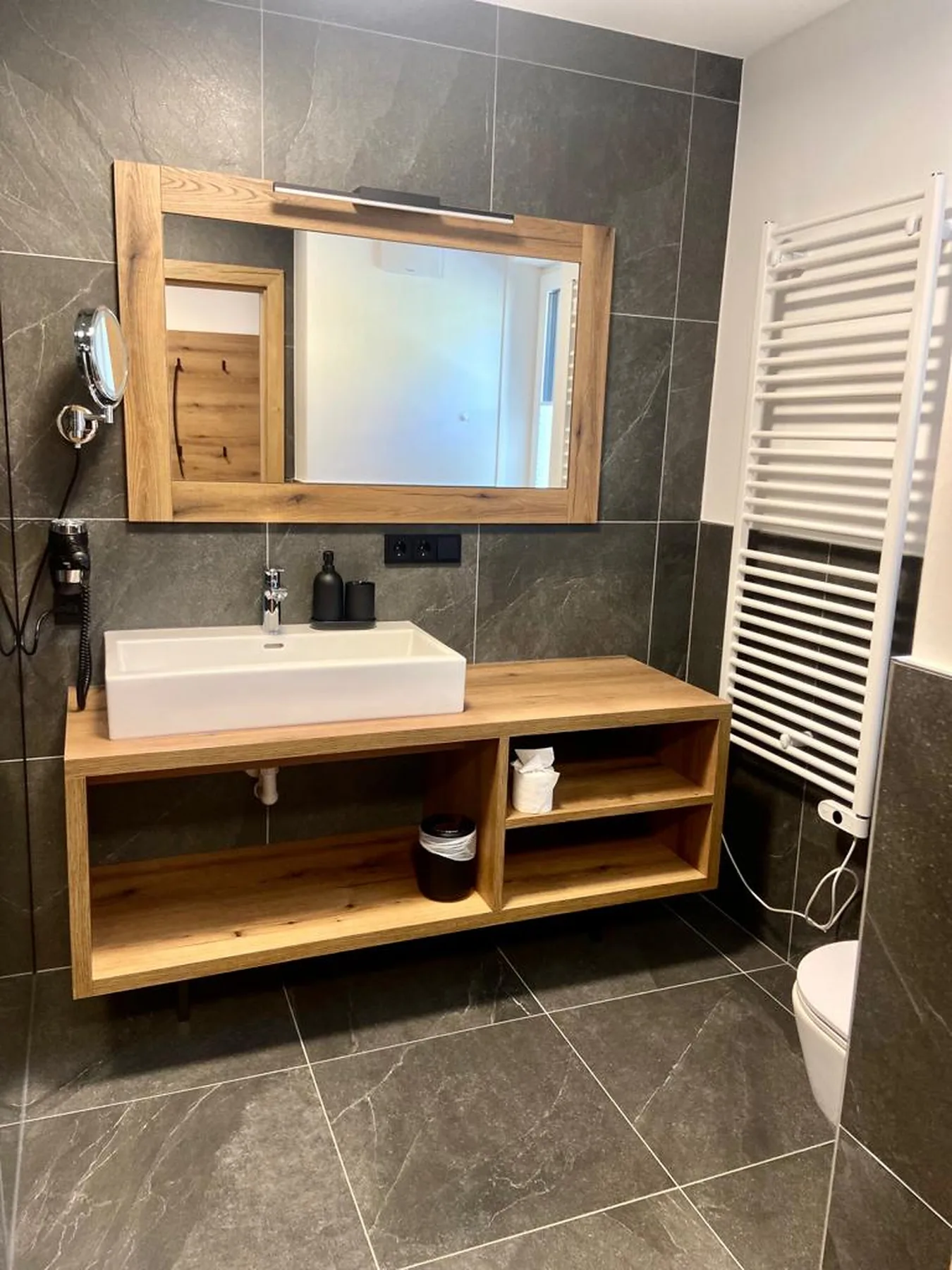 A tiled bathroom with a wood vanity, sink, and large mirror.