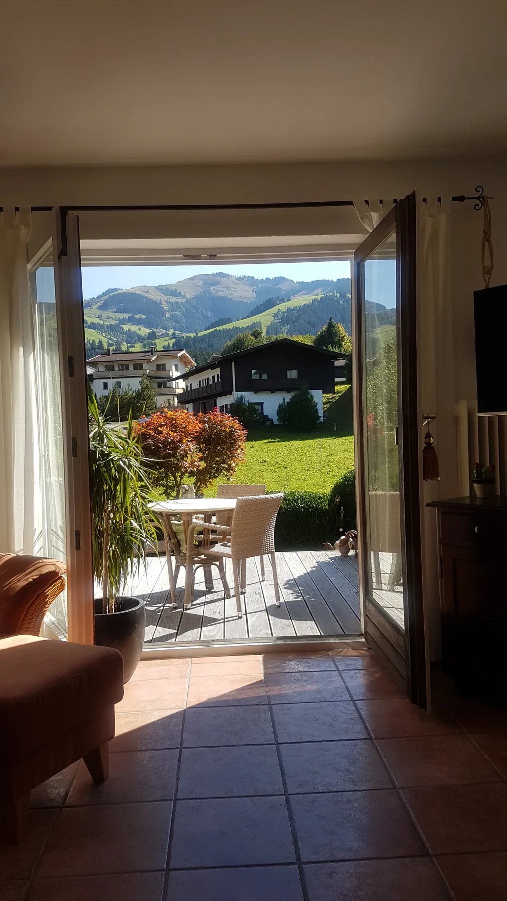Una puerta abierta da a un patio exterior con asientos y un jardín verde.