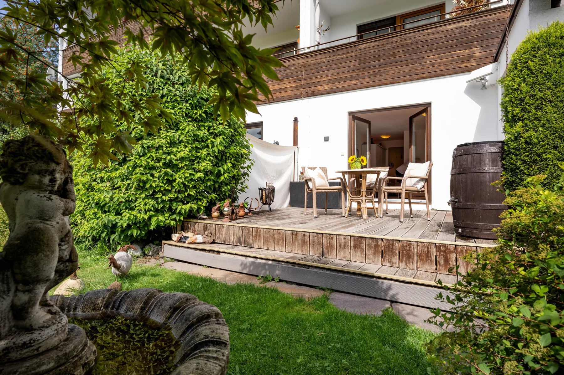 A garden patio with outdoor seating and a wooden deck beside the house.