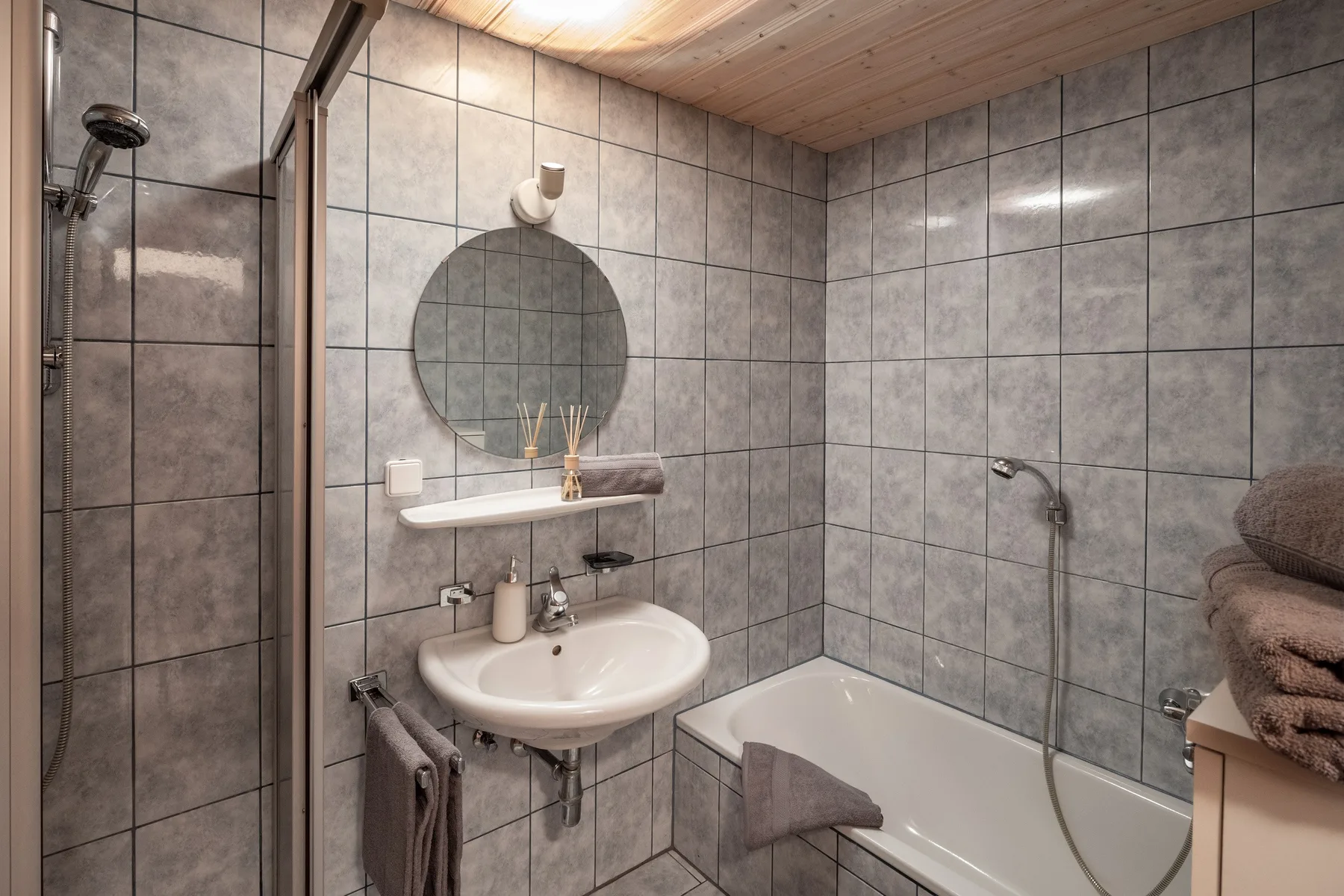 Un baño revestido de azulejos con lavabo, espejo redondo y bañera.