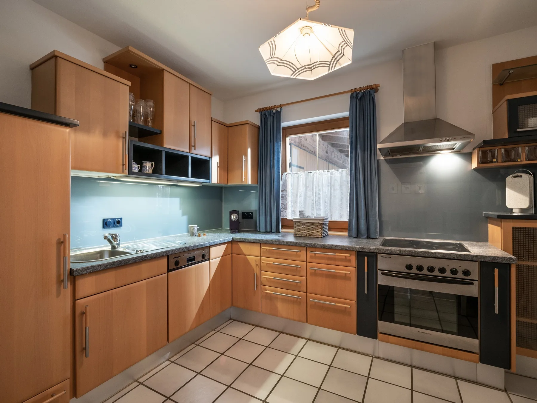 Una cocina con gabinetes de madera, suelo de baldosas y una ventana central.