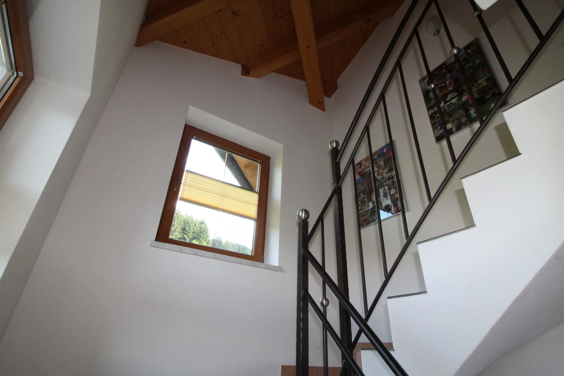 A staircase with dark metal railings rises beside a window.