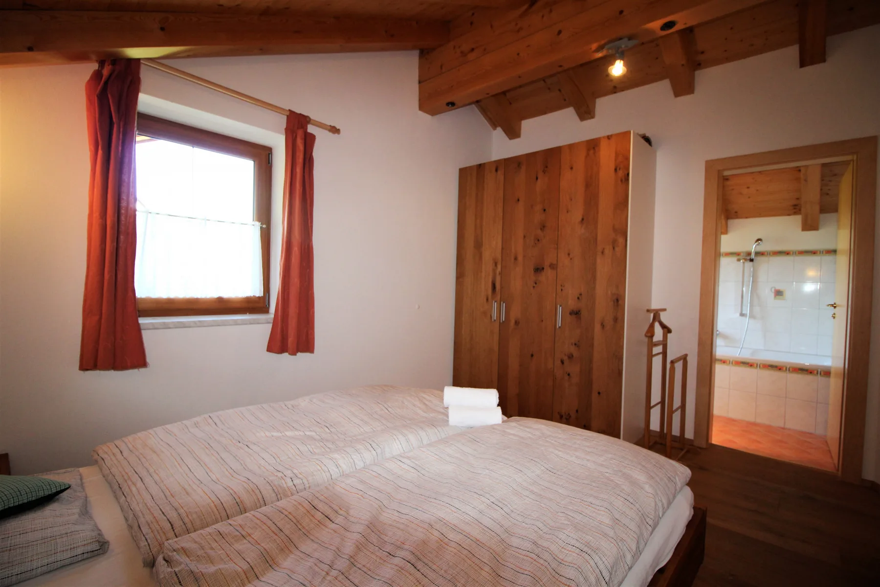 A bedroom with two beds, a wooden wardrobe, and a curtained window.