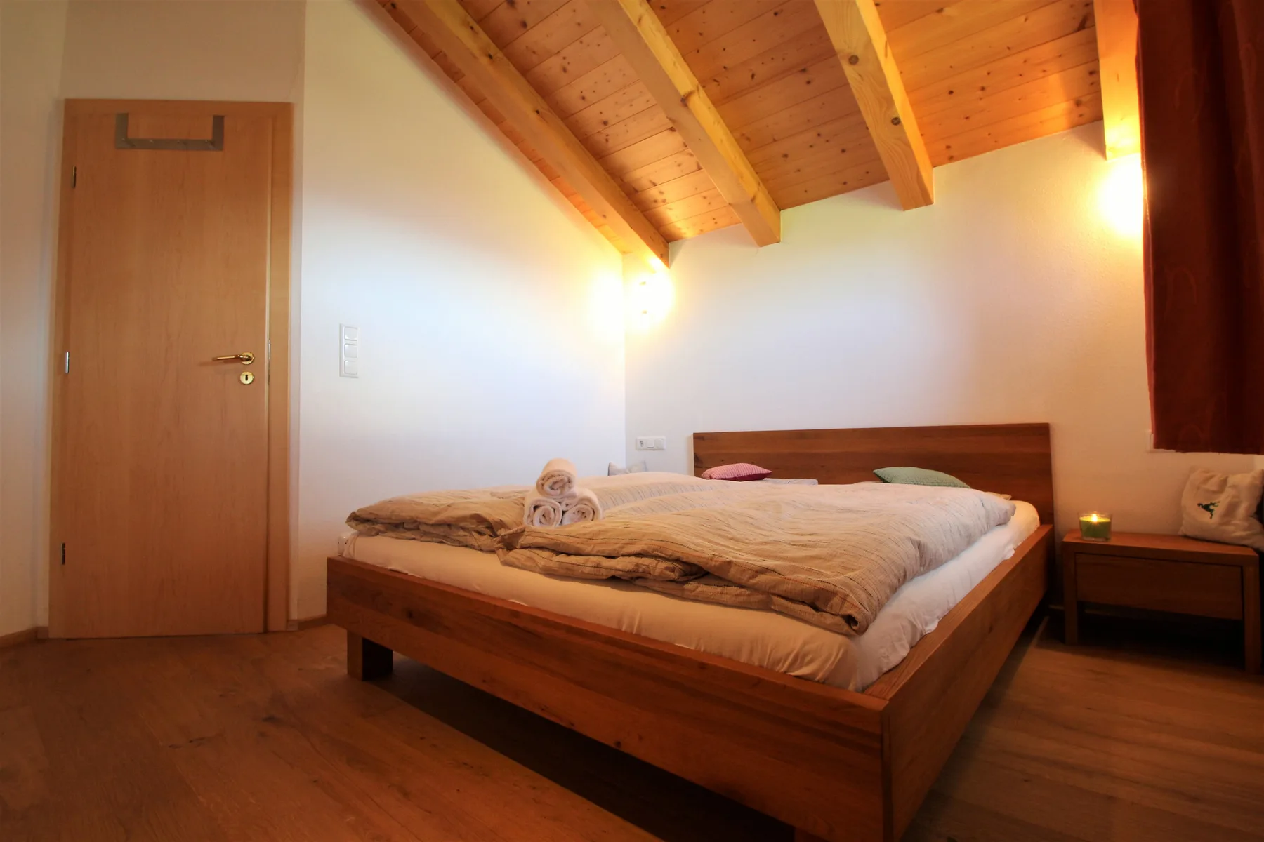 A bedroom with a wooden bed beneath a sloped timber ceiling.