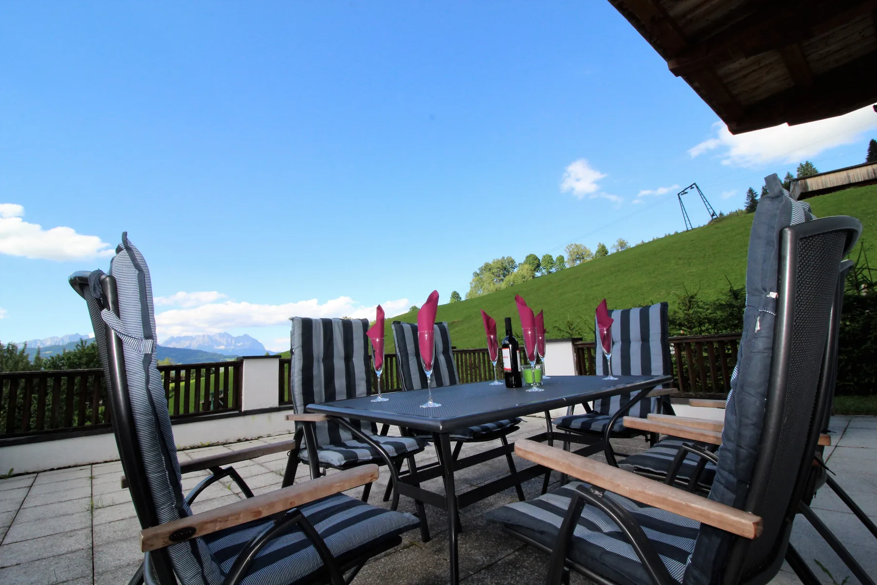 An outdoor dining area with a table and seating overlooks a grassy hillside.