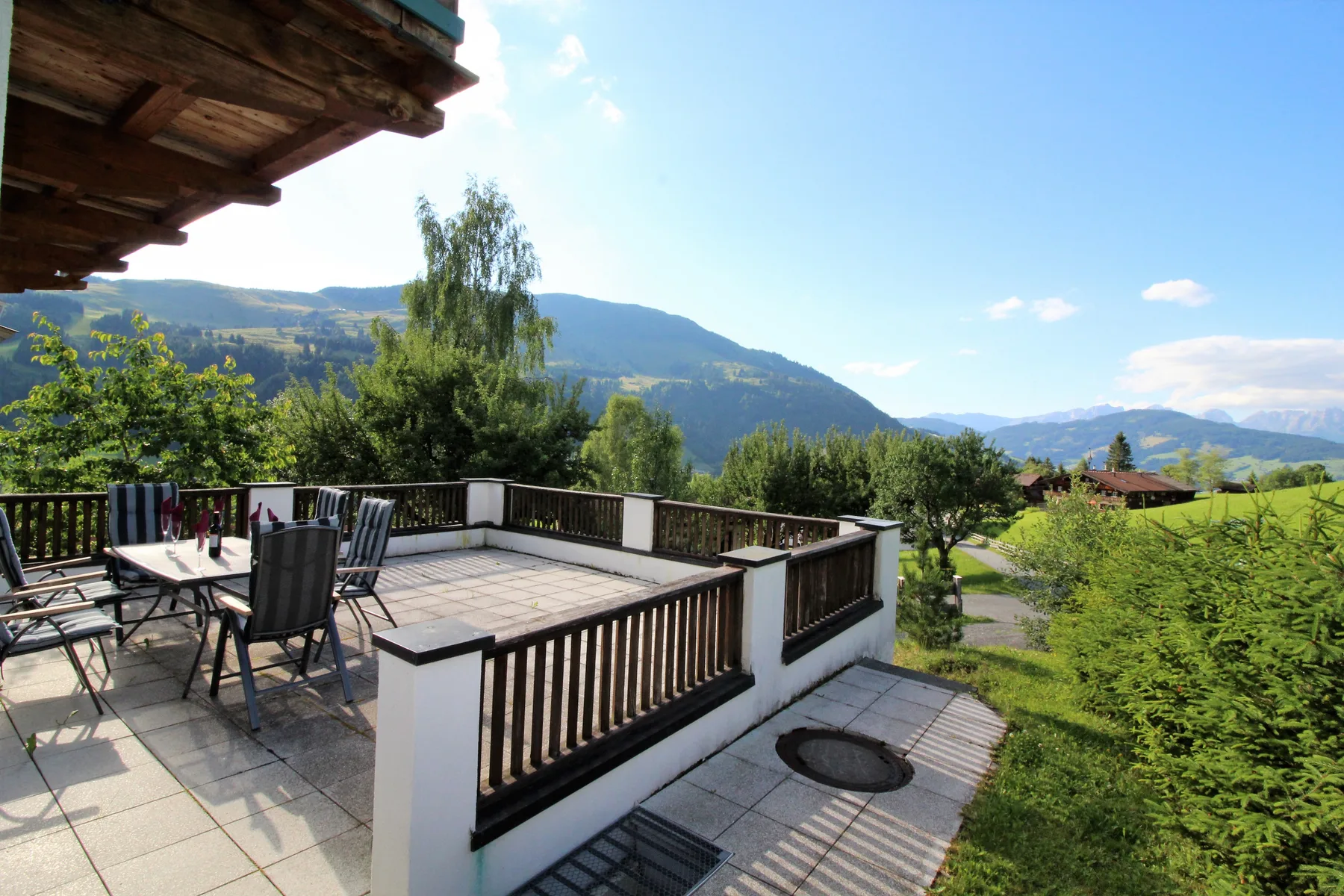 An outdoor terrace with seating overlooks green hills and a mountain range.