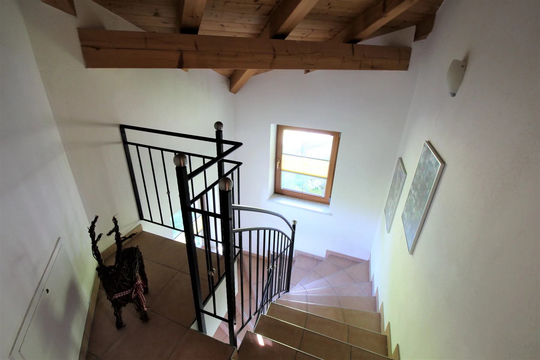 An interior staircase with dark railings descends beneath exposed wooden ceiling beams.