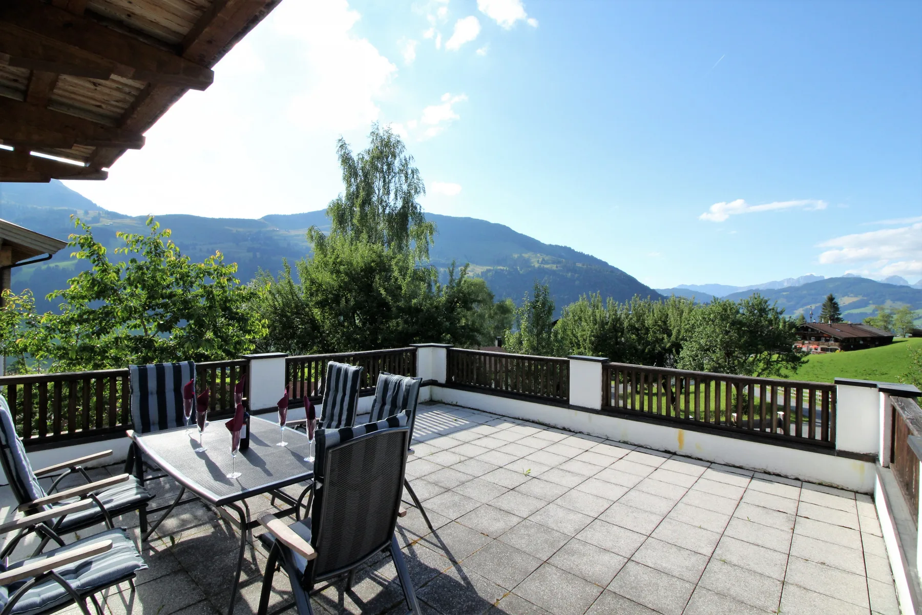 A tiled outdoor terrace has seating and views of green hills.