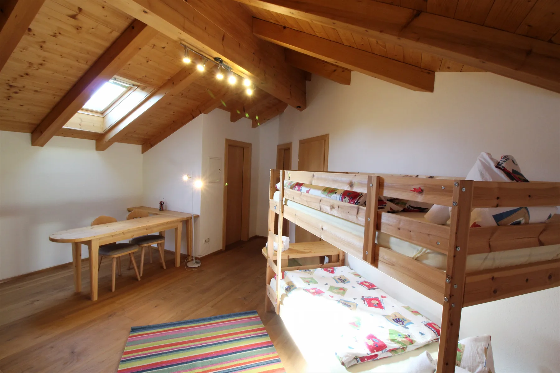 A loft bedroom with wooden bunk beds, a skylight, and a small table.