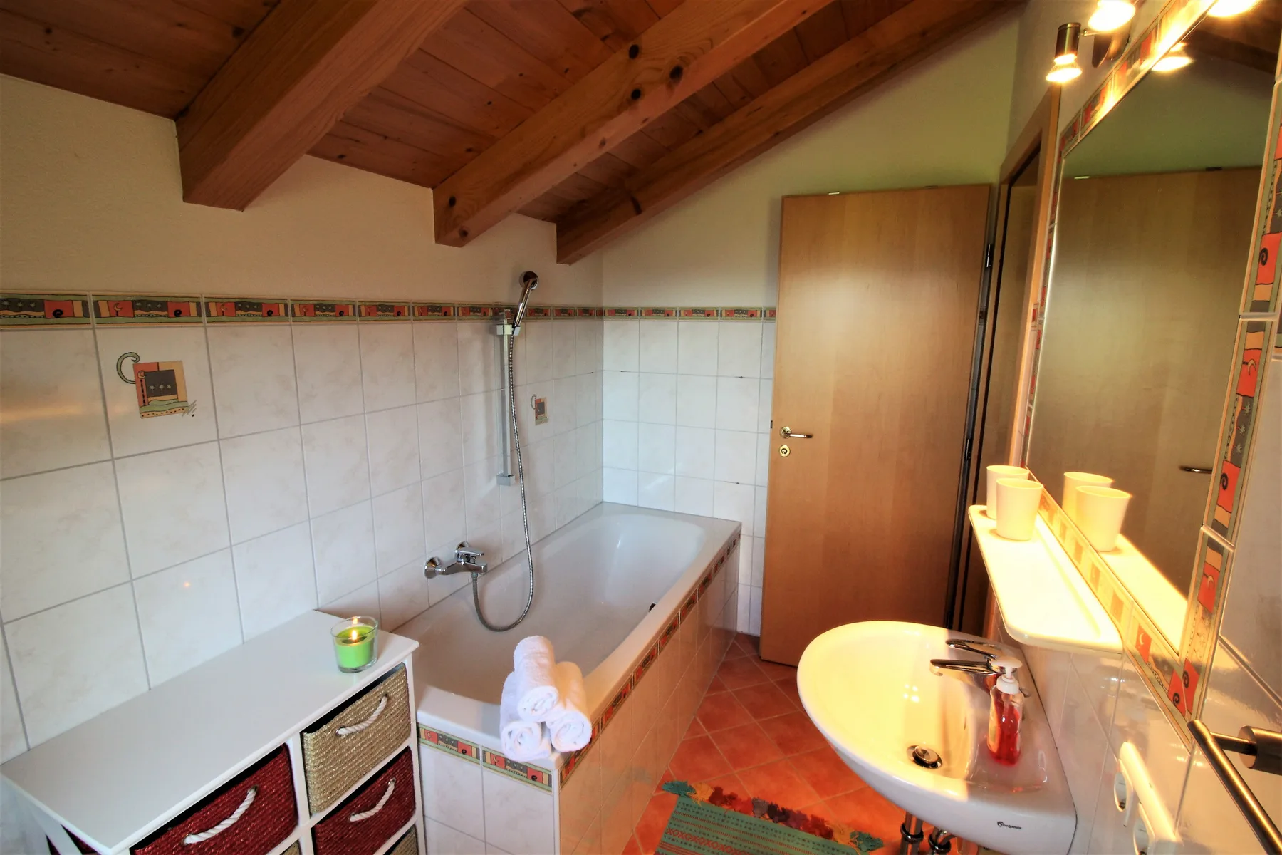 A tiled bathroom with a bathtub, sink, and sloped wooden ceiling.