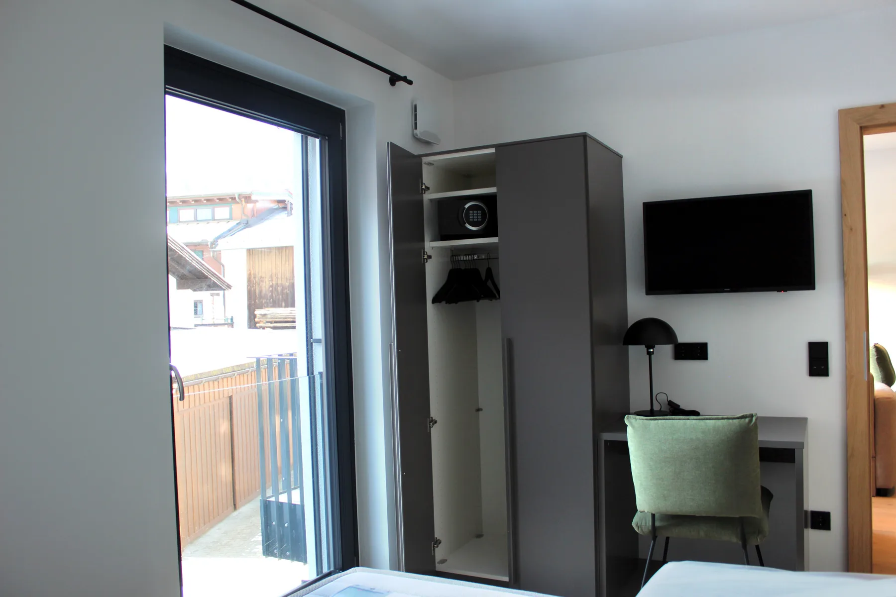 Un dormitorio compacto con armario, televisor en la pared y una ventana grande.