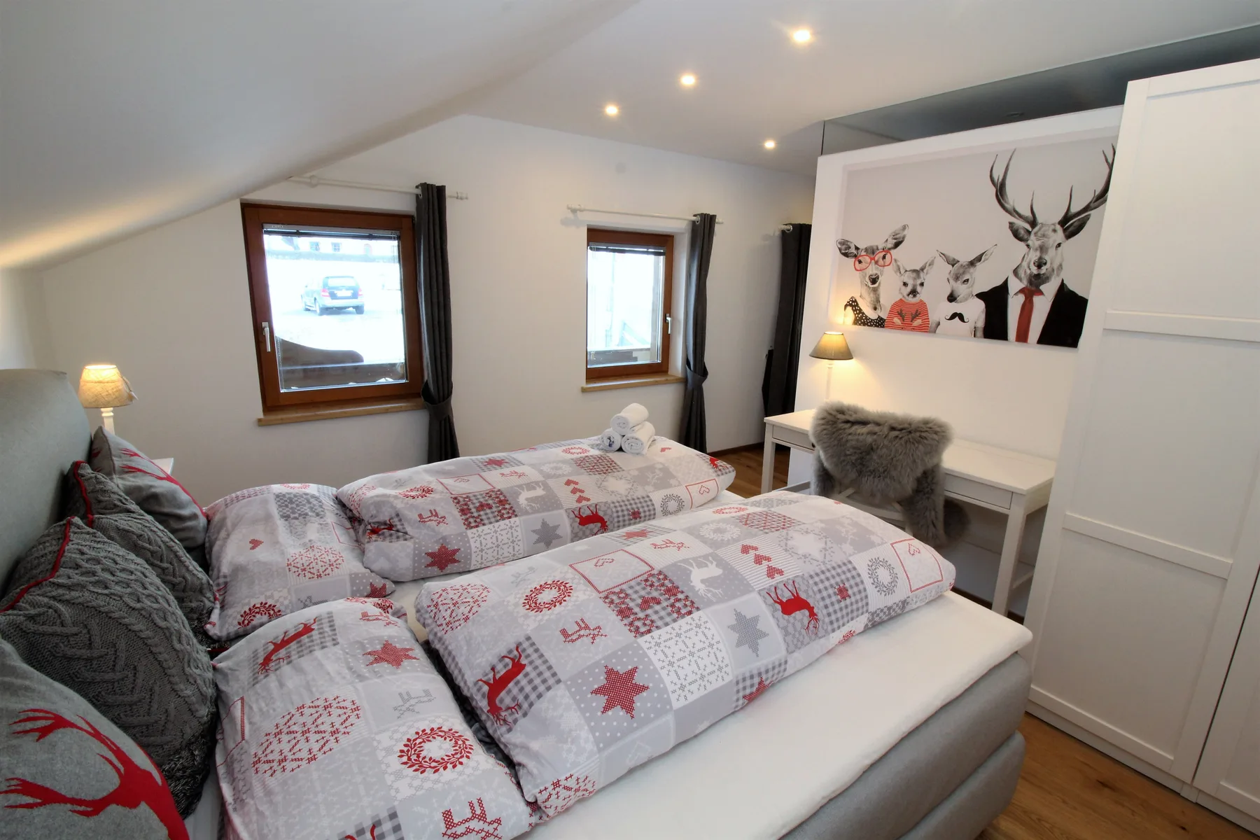 A bedroom with patterned bedding, sloped ceilings, and two windows.