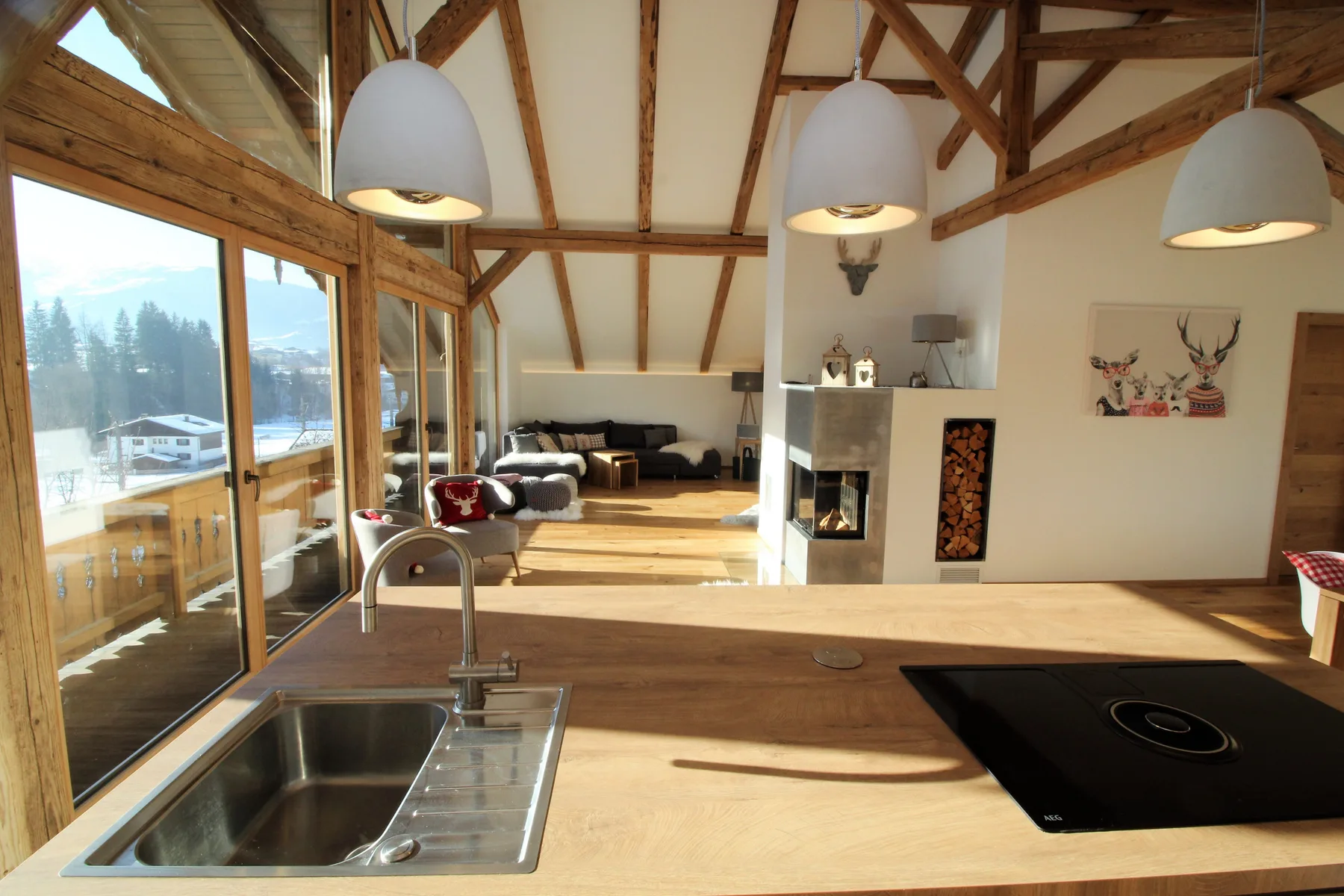 A bright open-plan kitchen and living area with large windows and exposed wooden beams.