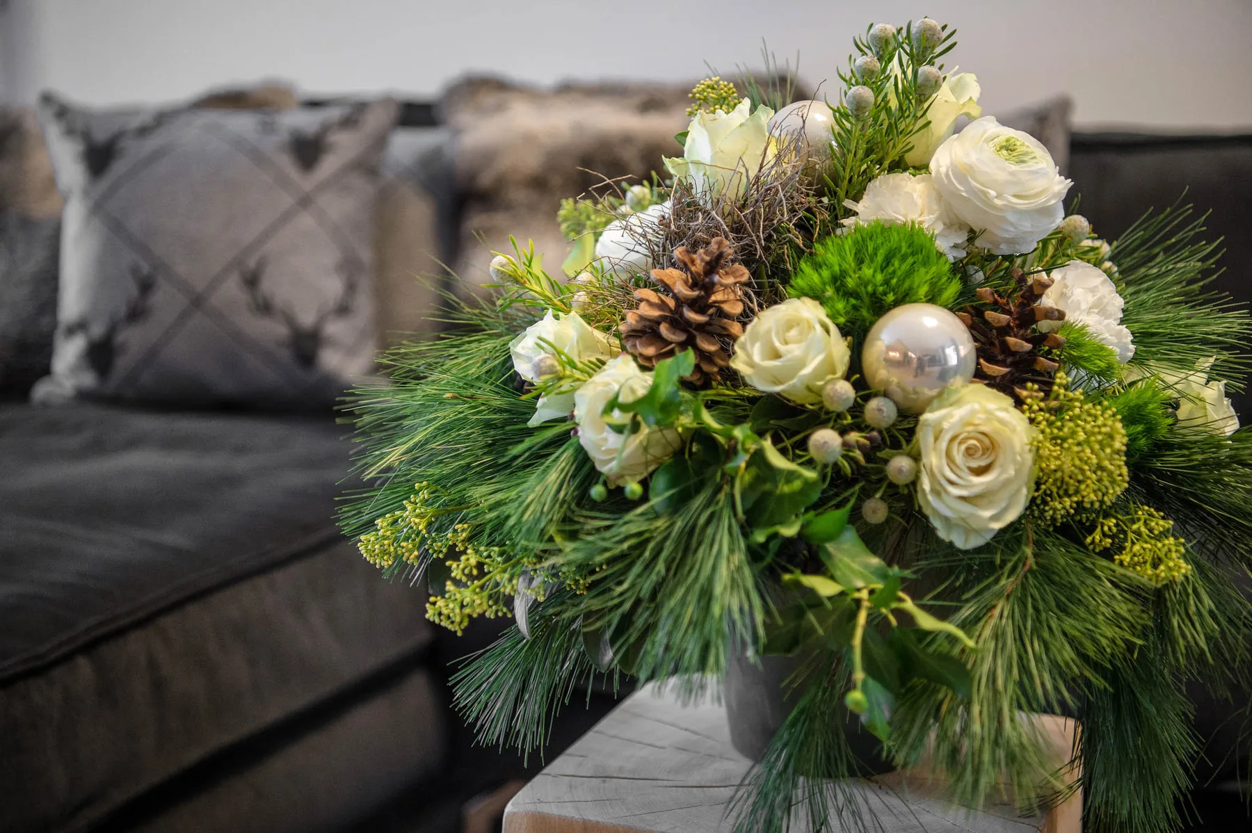 Un arreglo floral con rosas blancas y follaje está junto a unos asientos oscuros.