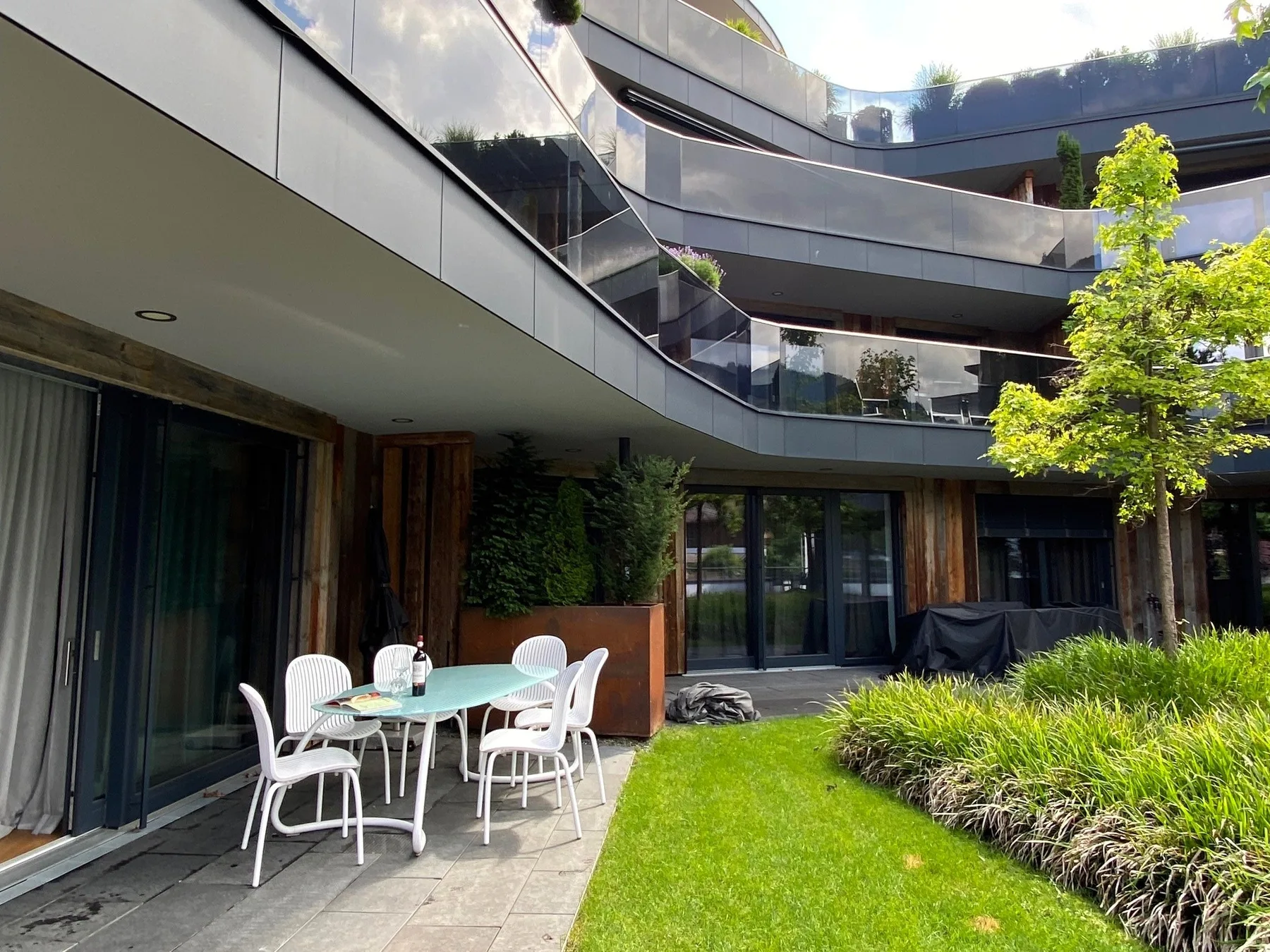 Un patio moderno con césped, asientos al aire libre y balcones curvos.