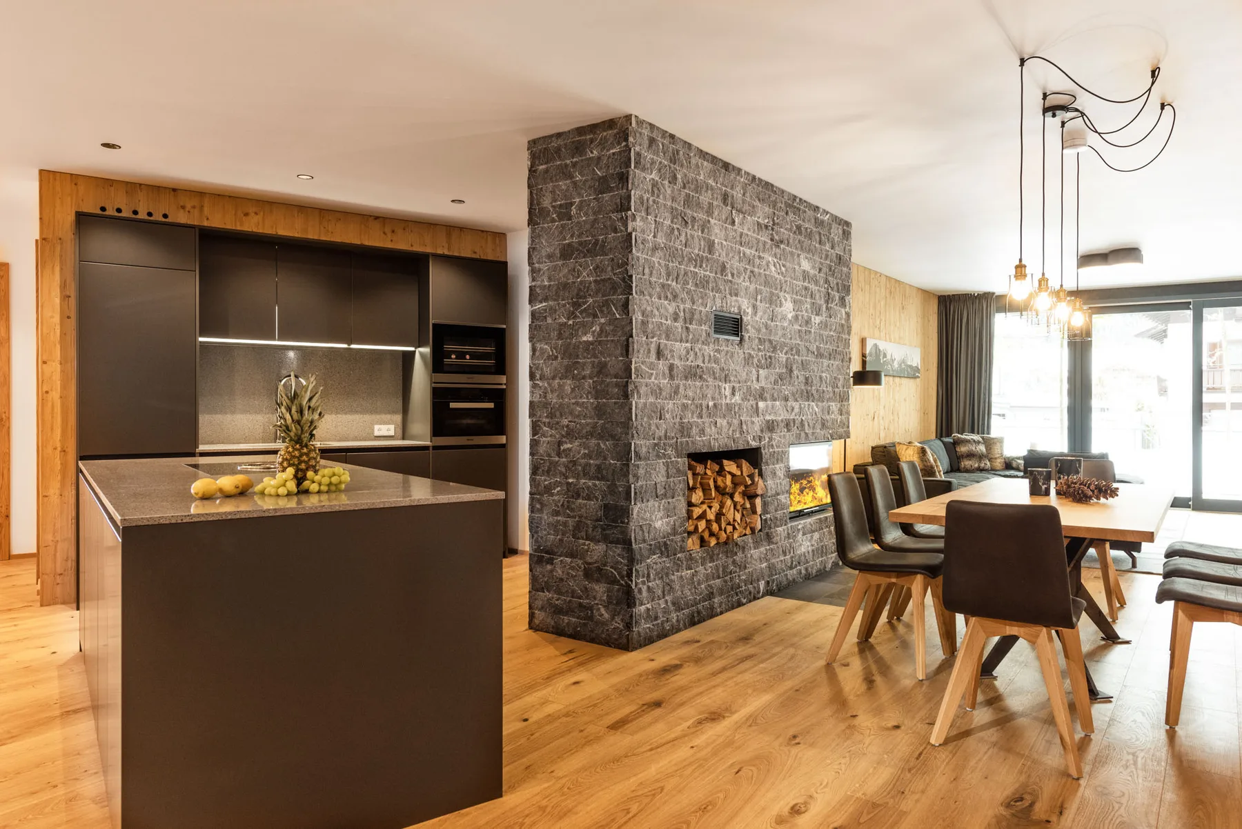Una cocina y comedor de concepto abierto con una chimenea de piedra y suelo de madera.