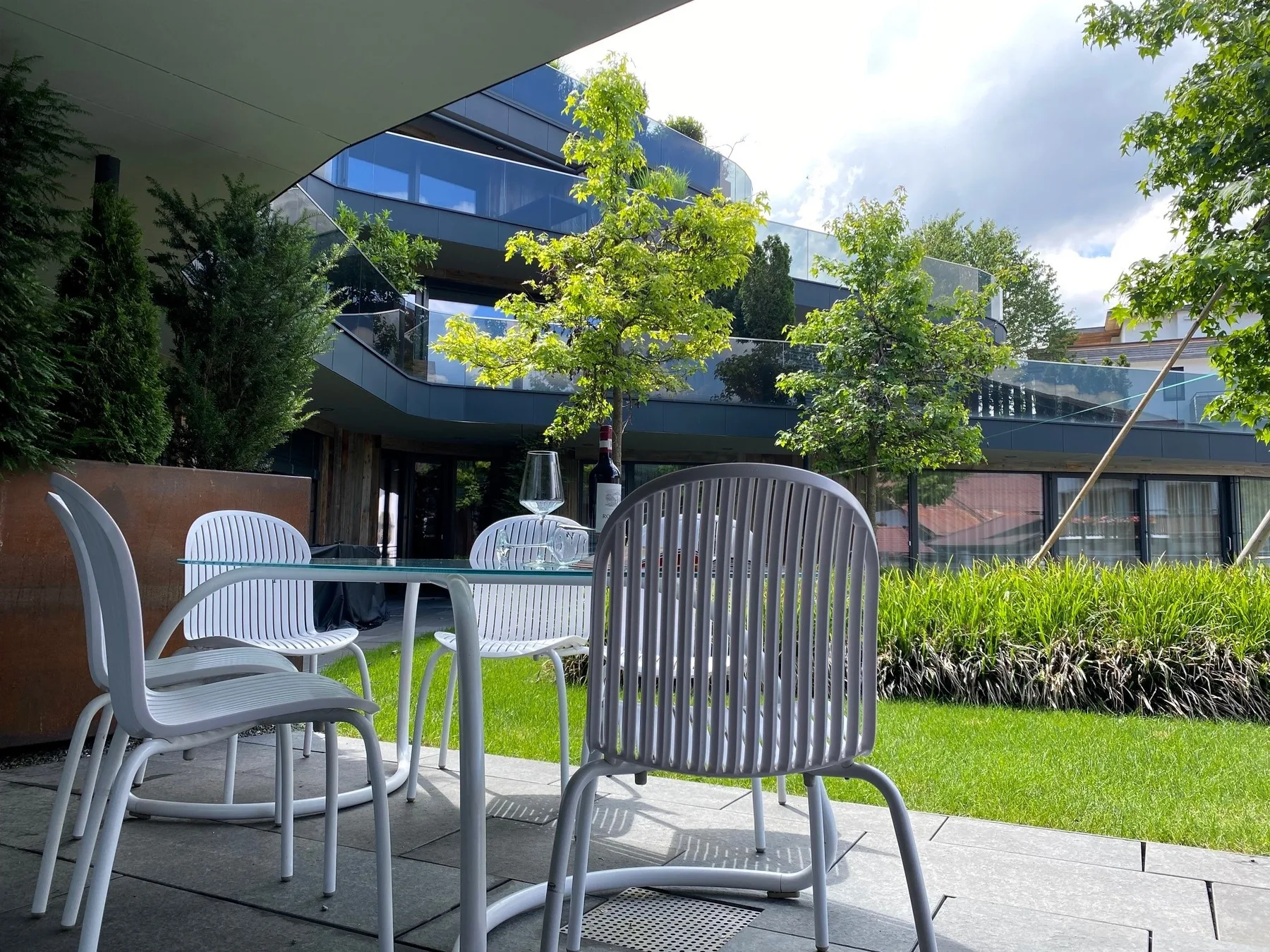 Un patio exterior con asientos metálicos junto a un césped y un edificio moderno.