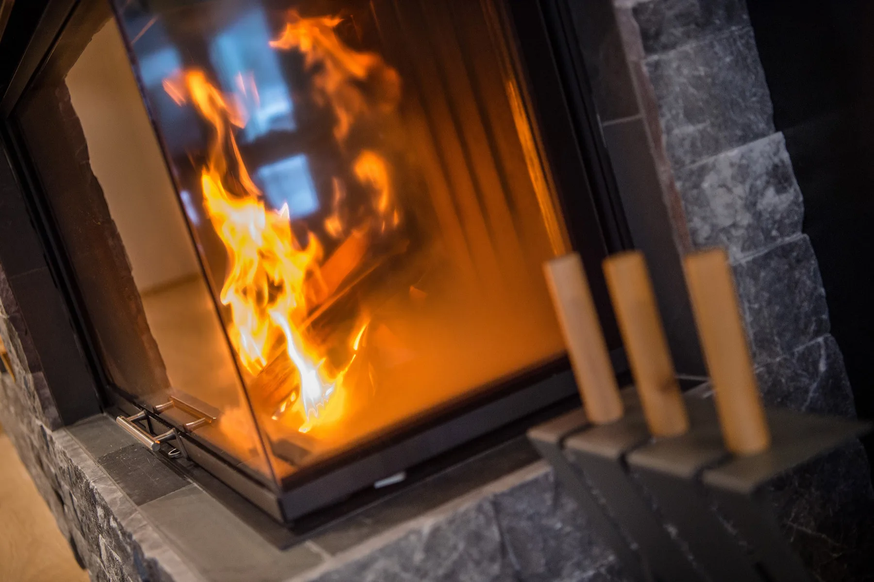 Una chimenea con frente de vidrio arde junto a un revestimiento de piedra oscura.